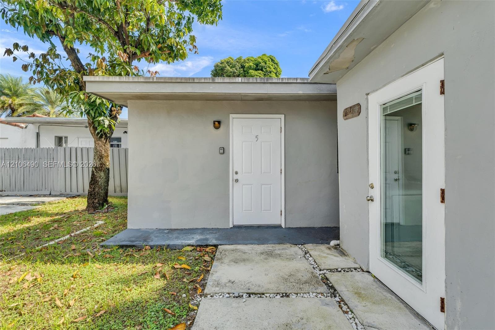 Exterior facade featuring smooth stucco siding, flat roofline with an overhang, concrete paver walkway, and glass-paneled entry door