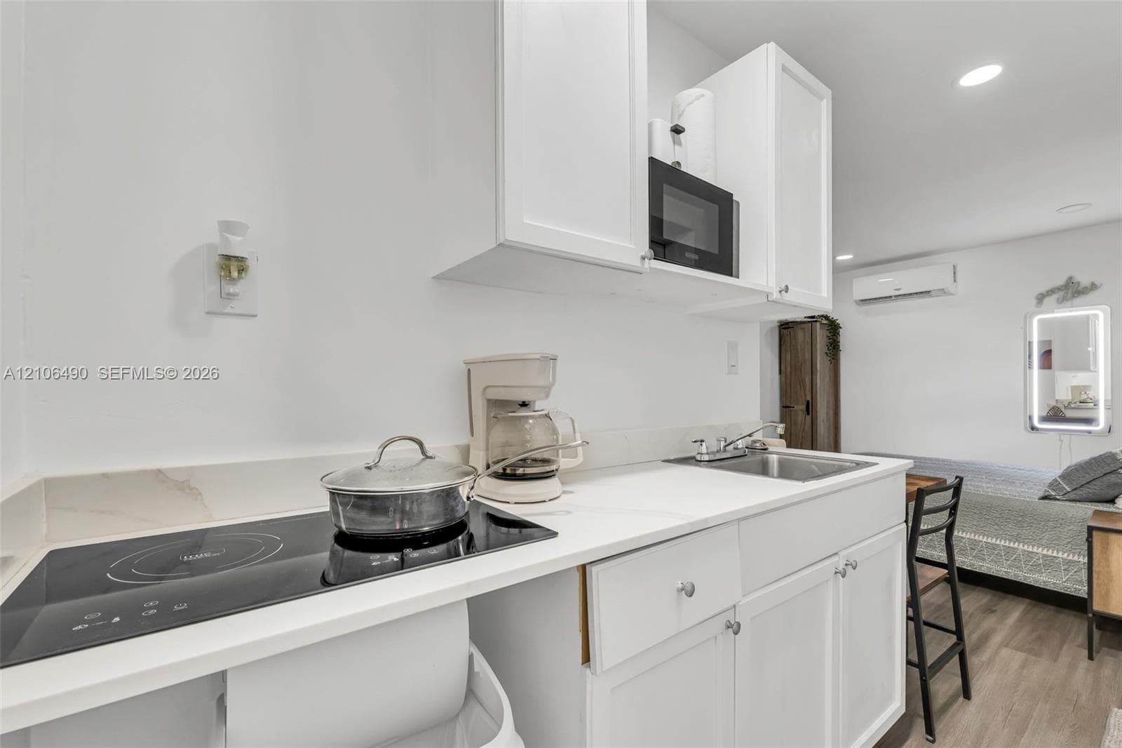 White cabinetry, solid-surface countertops, integrated cooktop, stainless steel sink with a metallic faucet, and wood-finish flooring