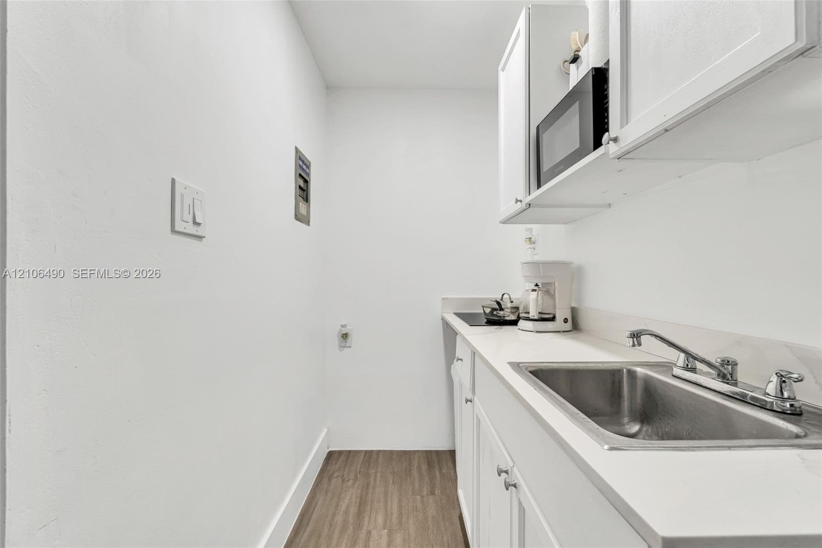 Kitchenette area featuring white cabinetry, solid-surface countertops, an undermount stainless steel sink, and wood-finish flooring