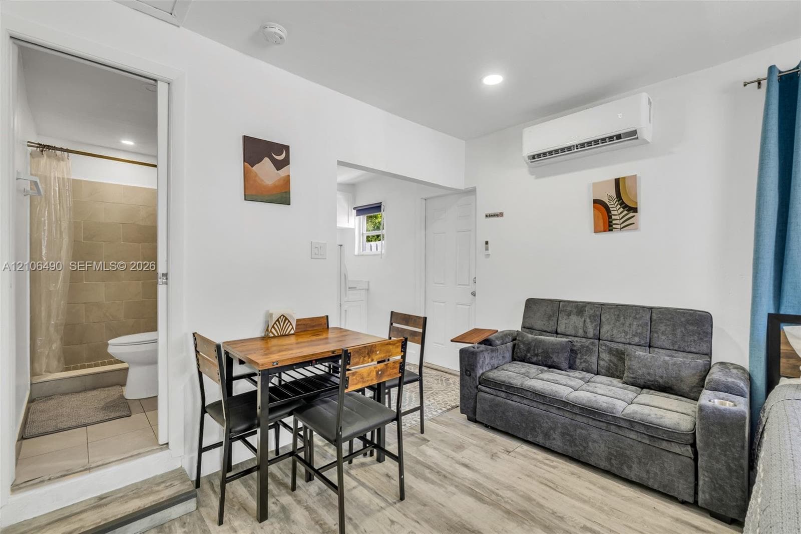 Wood-finish flooring, wall-mounted ductless air conditioning unit, recessed lighting, and a bathroom featuring a walk-in shower with neutral tile surround