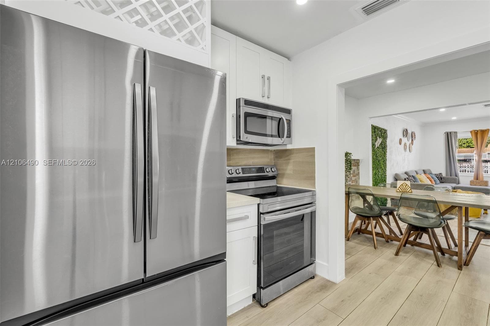 Kitchen featuring stainless steel appliances, white cabinetry with built-in wine storage, wood-finish flooring, and a neutral tile backsplash
