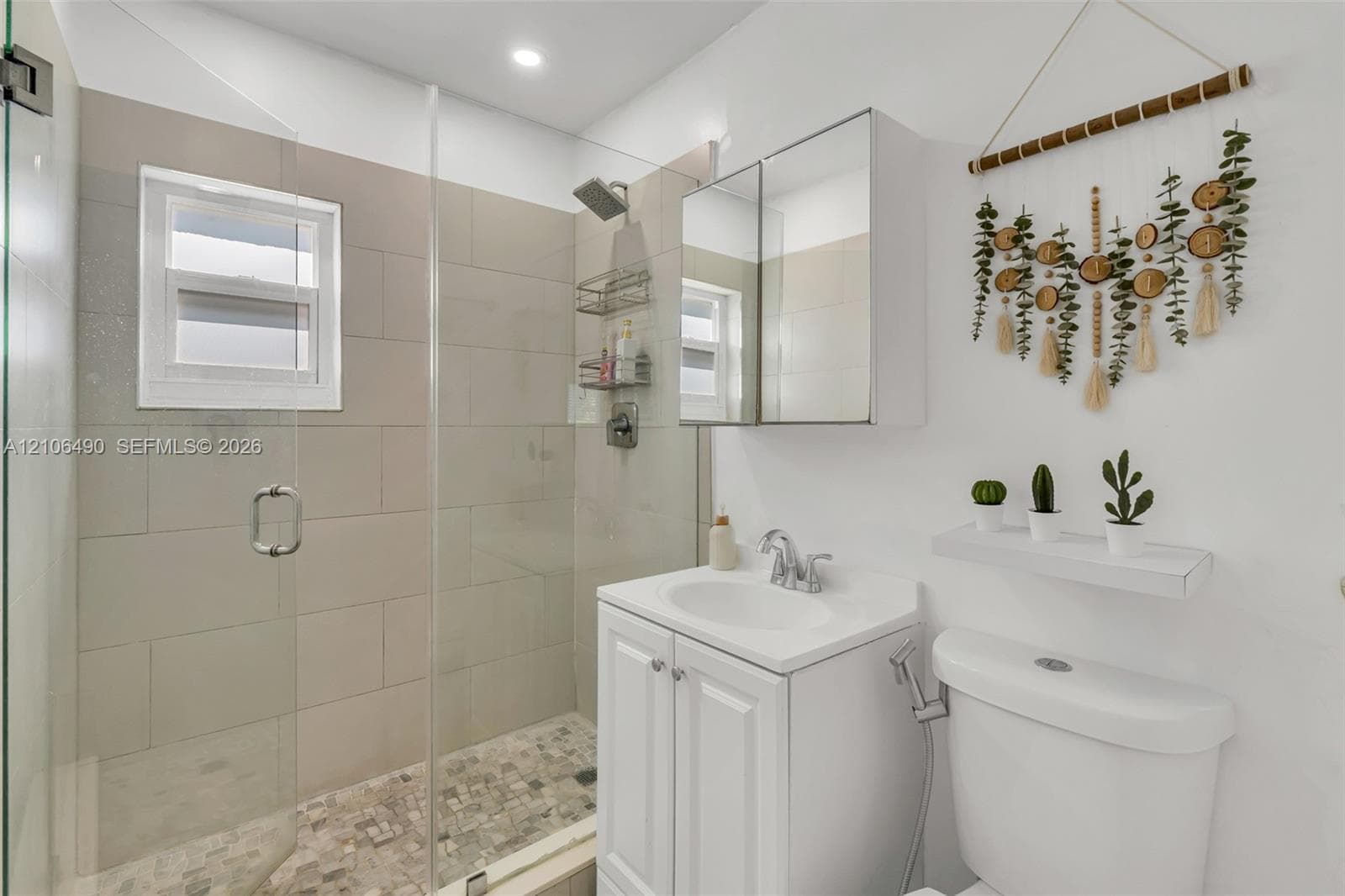 Bathroom featuring a glass-enclosed shower with large-format tile surround, stone-tiled shower floor, white vanity cabinet with integrated sink, and mirrored medicine cabinet
