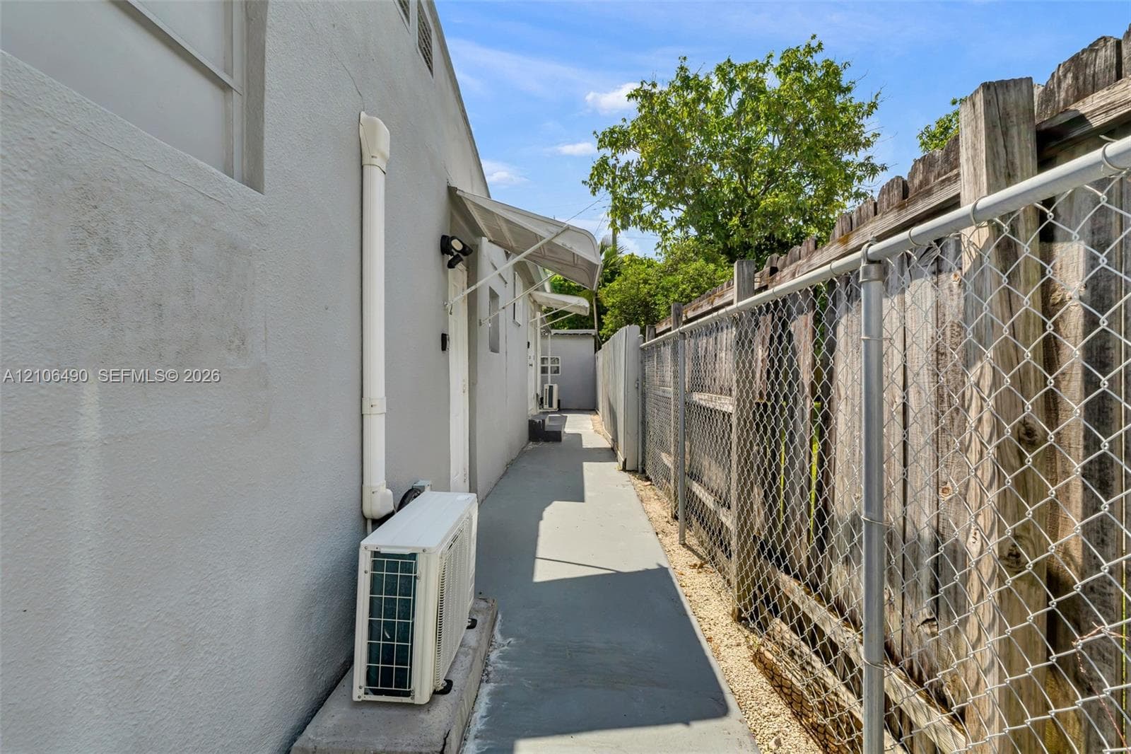 Side exterior featuring a concrete pathway, metal chain-link fencing, wood privacy fencing, and exterior wall-mounted awnings