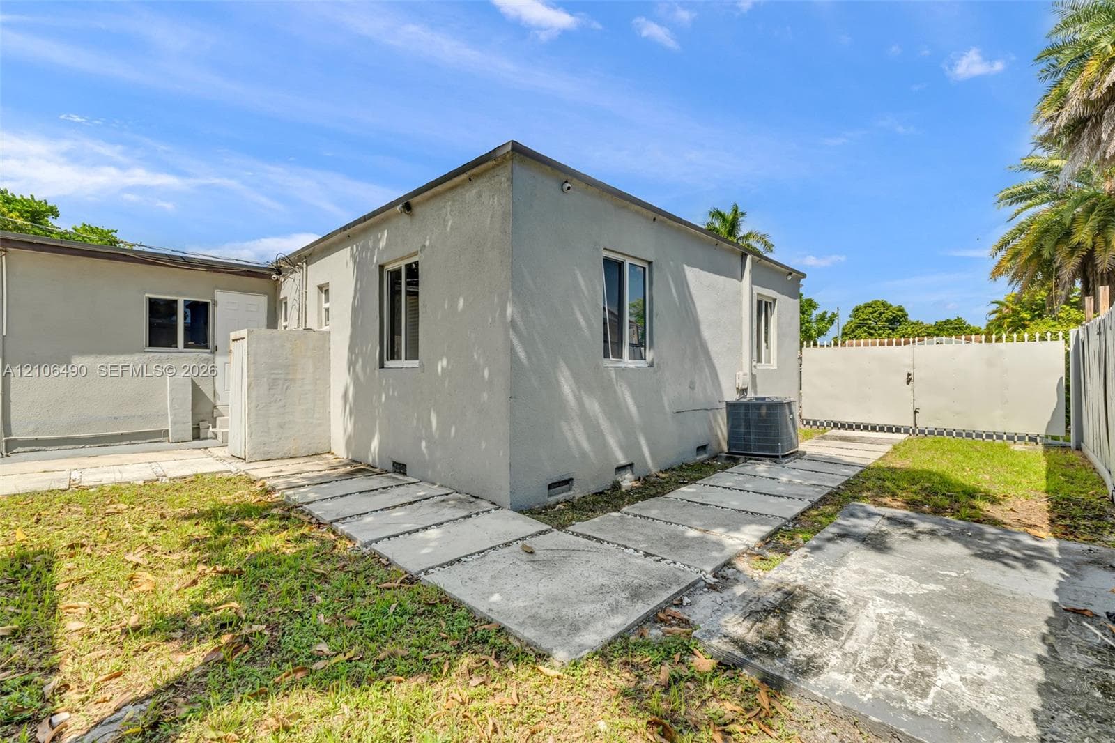 Stucco exterior featuring concrete paver pathways, metal perimeter fencing, and a grass lawn