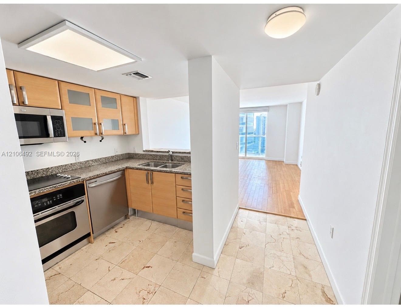 Kitchen featuring stone countertops, stainless steel appliances, light-toned cabinetry with glass-panel upper doors, stone tile flooring, and wood-finish flooring in the adjacent area