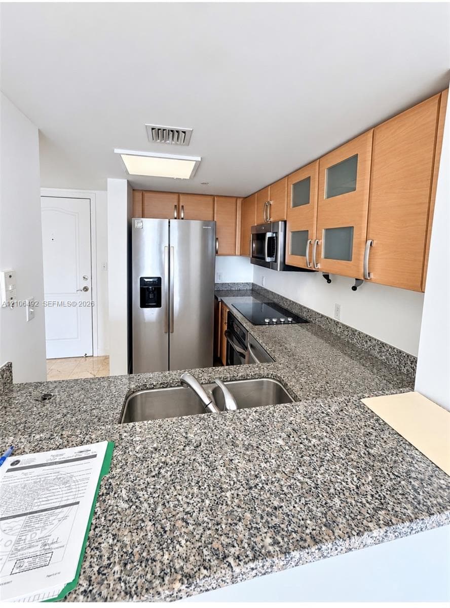 Kitchen featuring wood cabinetry, stone countertops, stainless steel appliances, and a dual-basin undermount sink
