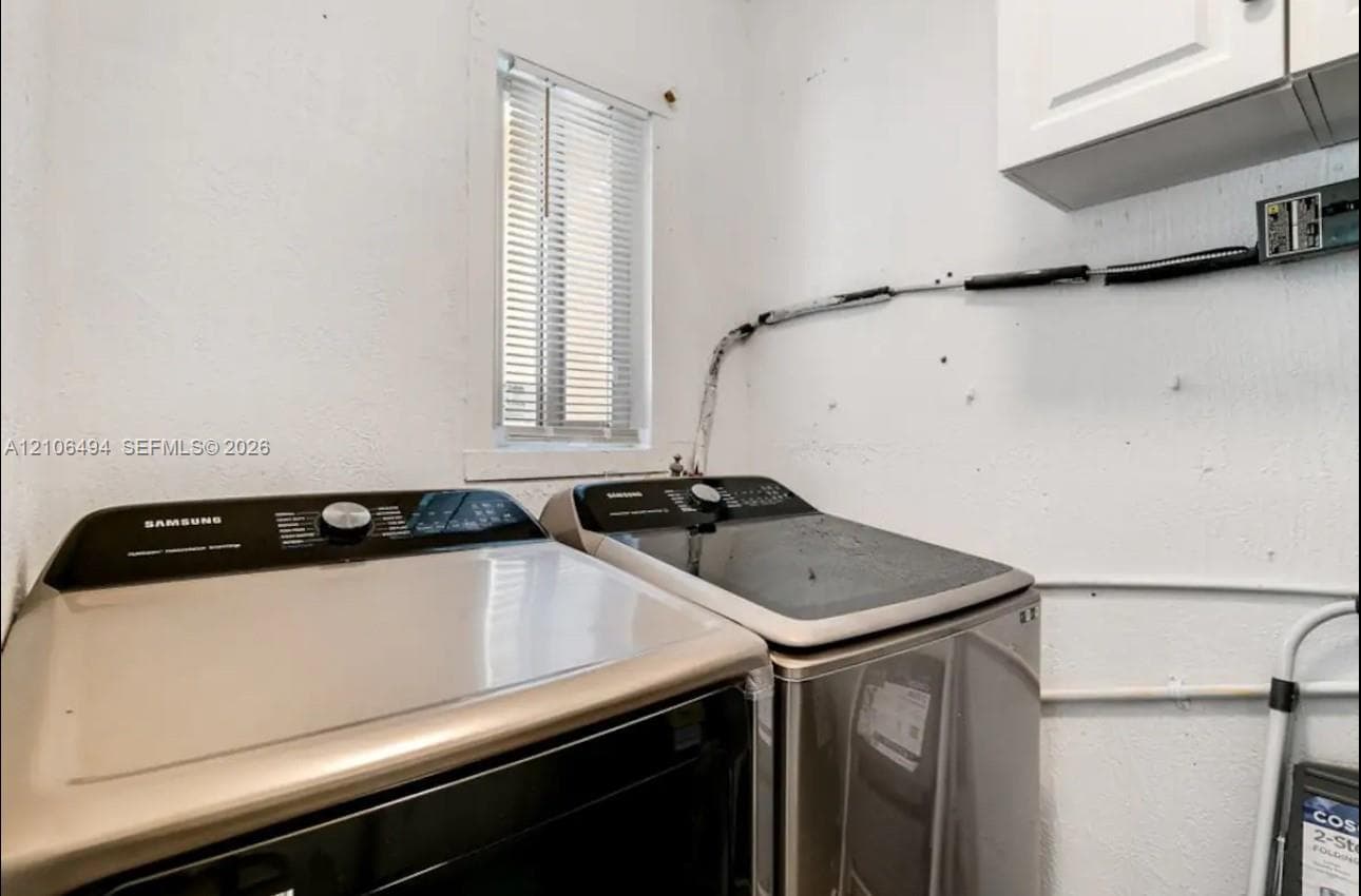 Utility room featuring wall-mounted white cabinetry and an operable window with horizontal blinds