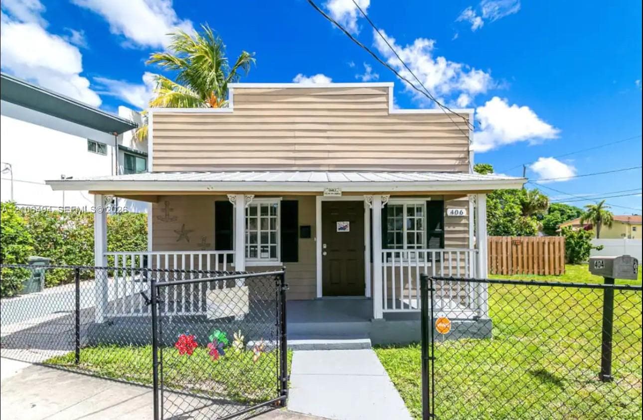 Single-story residence featuring horizontal lap siding, a metal-roofed covered front porch with decorative millwork, grid-pane windows with shutters, and a gated chain-link fence