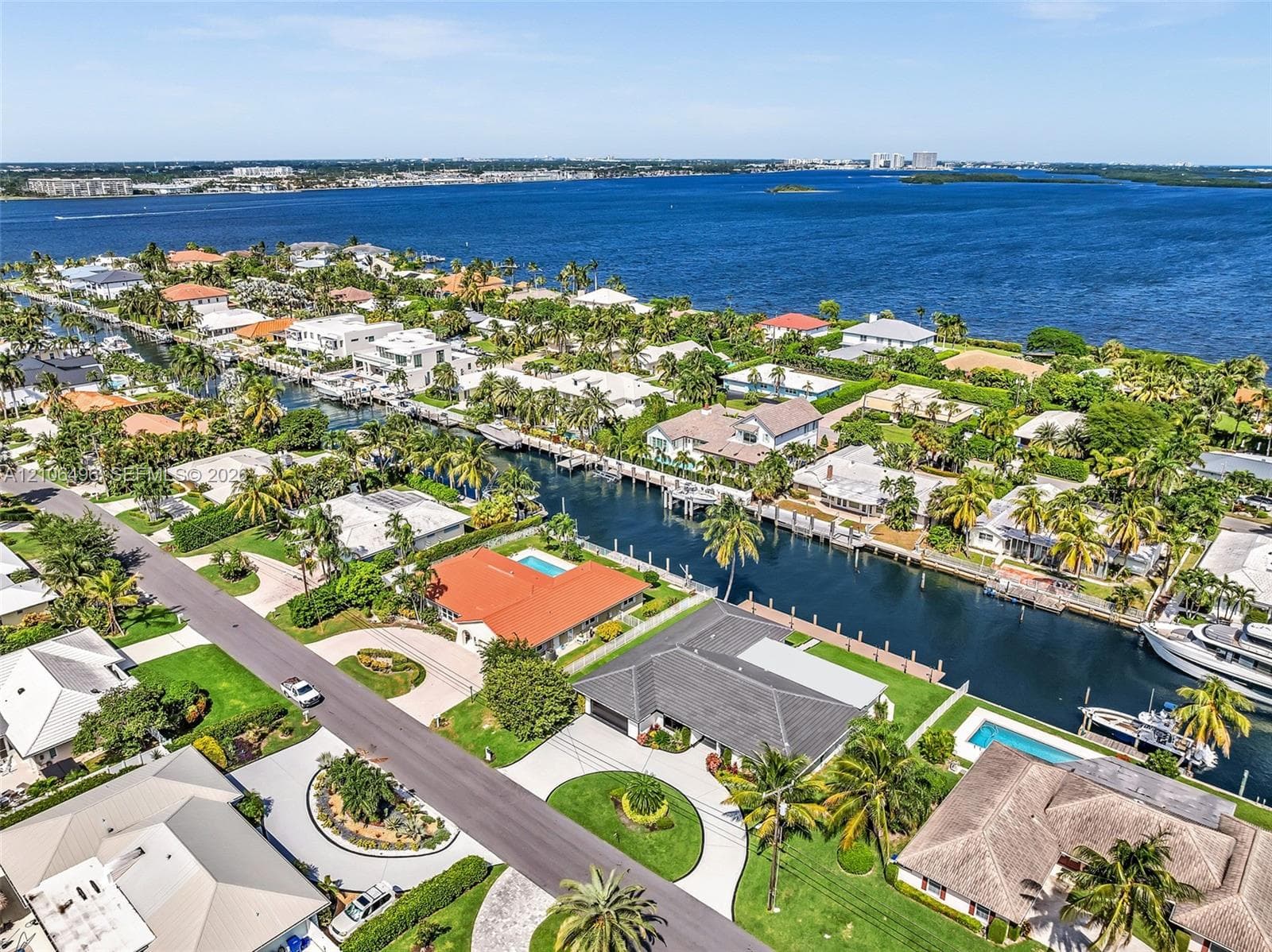 Aerial perspective of a coastal neighborhood featuring deep-water canal access, private boat docks, residential swimming pools, mature palm landscaping, and proximity to expansive open water