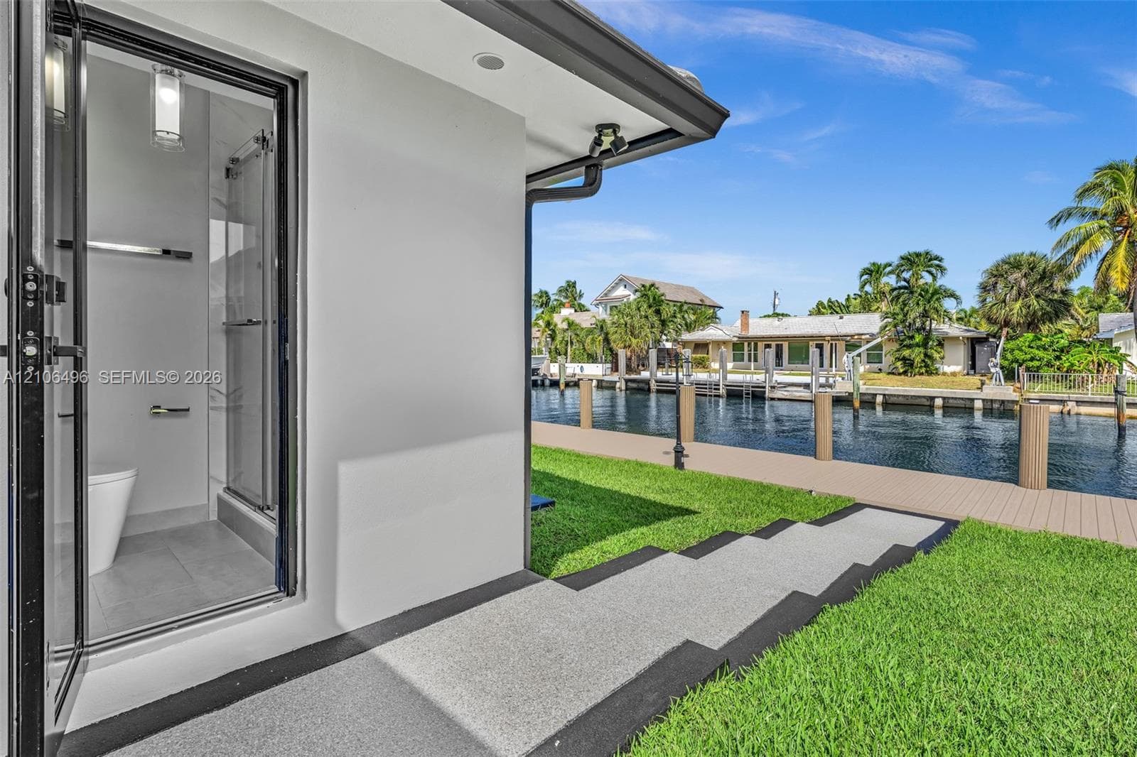 Exterior bathroom featuring a glass-enclosed shower, neutral-toned flooring, and modern fixtures, complemented by a composite dock, a concrete walkway, and direct water frontage