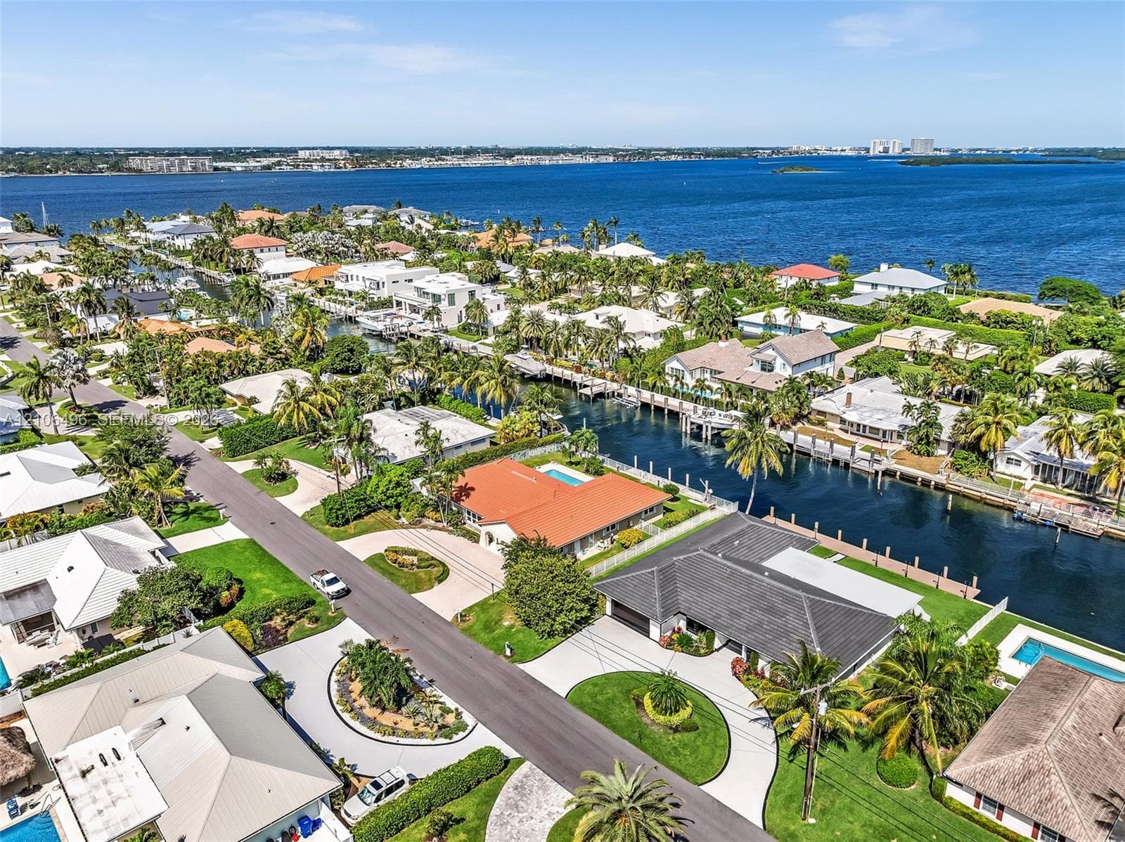 Aerial perspective of a waterfront property featuring a tile roof, paved circular driveway, landscaped lawn, and a private swimming pool