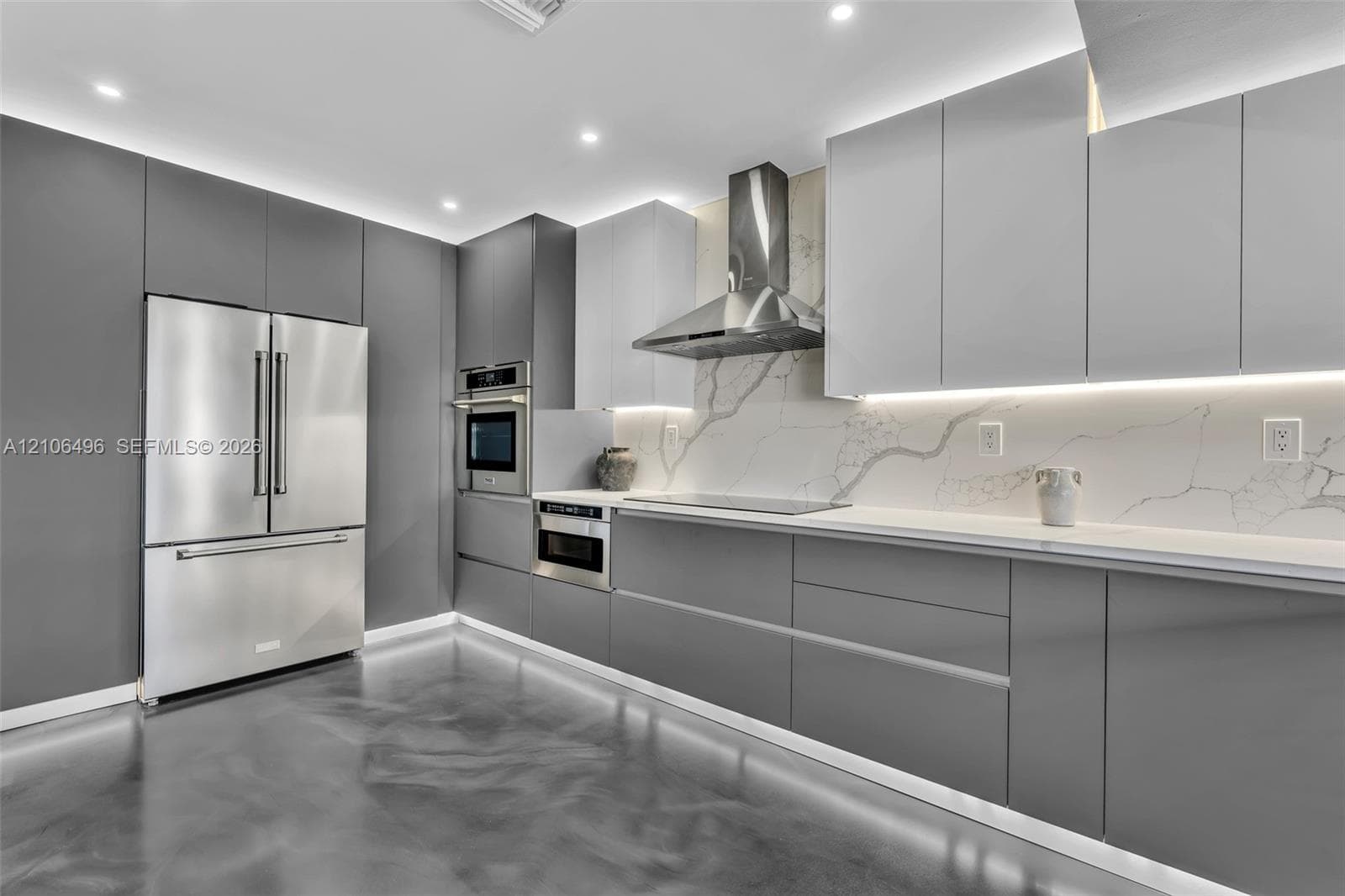 Kitchen featuring floor-to-ceiling cabinetry, stainless steel appliances, stone-surface backsplash, integrated under-cabinet lighting, and polished concrete flooring