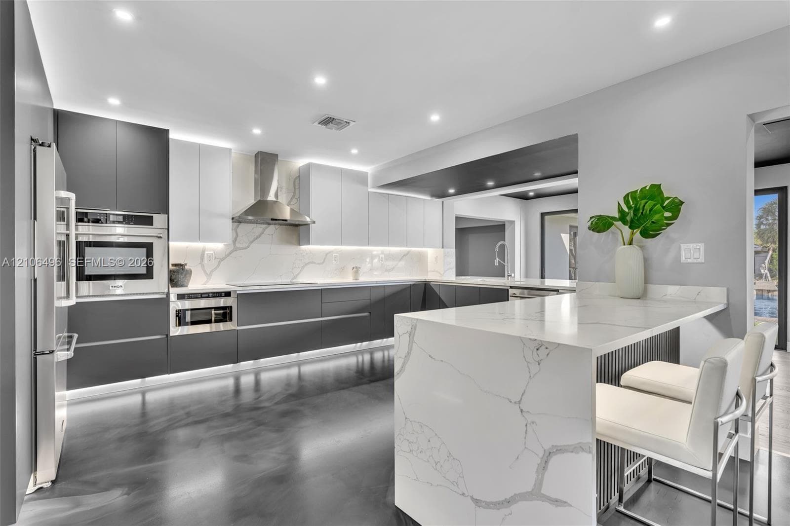 Kitchen featuring two-tone flat-panel cabinetry, a waterfall-edge stone countertop, integrated stainless steel appliances, and under-cabinet accent lighting