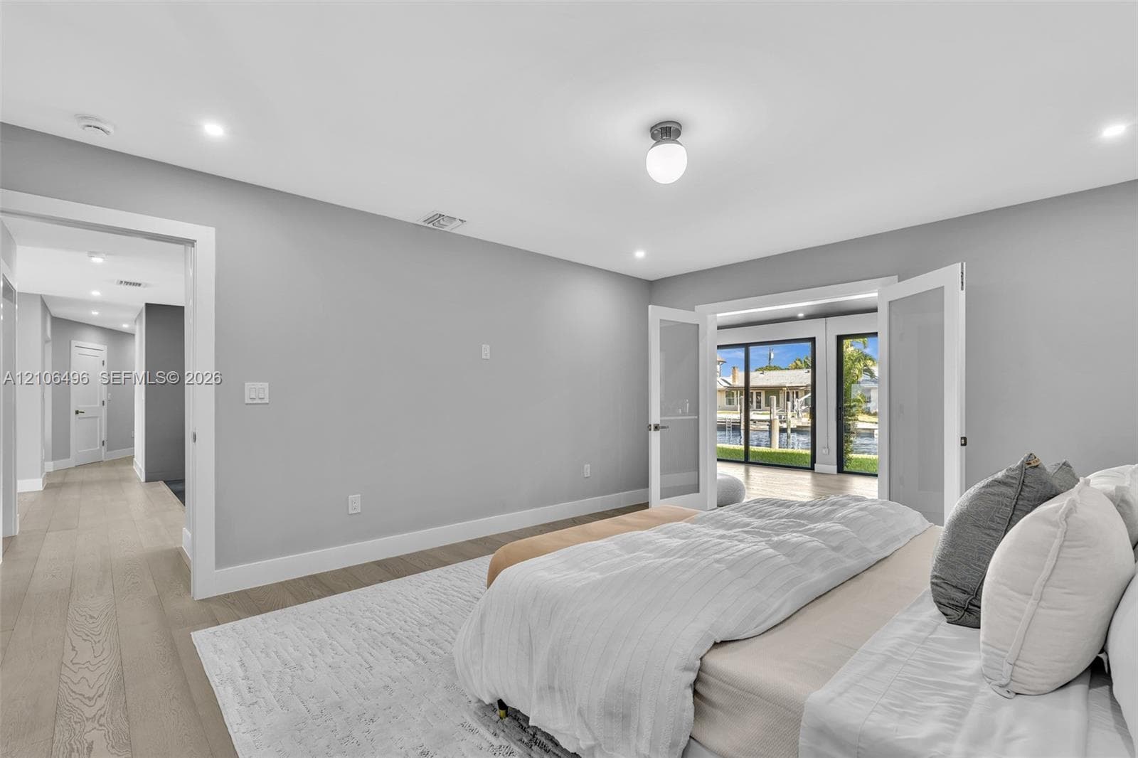 Neutral-toned interior featuring wood-finish flooring, recessed lighting, double glass-panel doors, and sliding glass doors with exterior water exposure