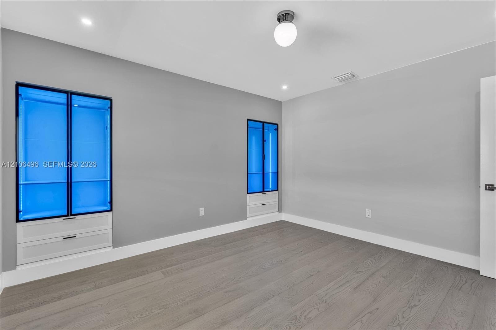 Wood-finish flooring, neutral wall tones, recessed lighting, and built-in cabinetry featuring illuminated glass-panel doors and integrated drawers