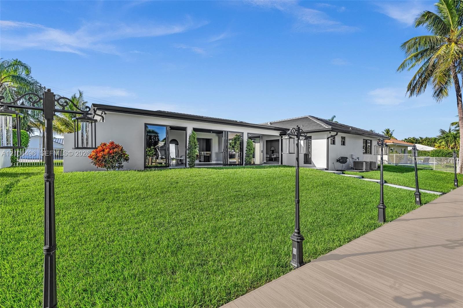 Exterior of a single-story residence featuring a smooth stucco facade, multi-panel sliding glass doors, a wide composite deck, and custom post-mounted exterior lighting