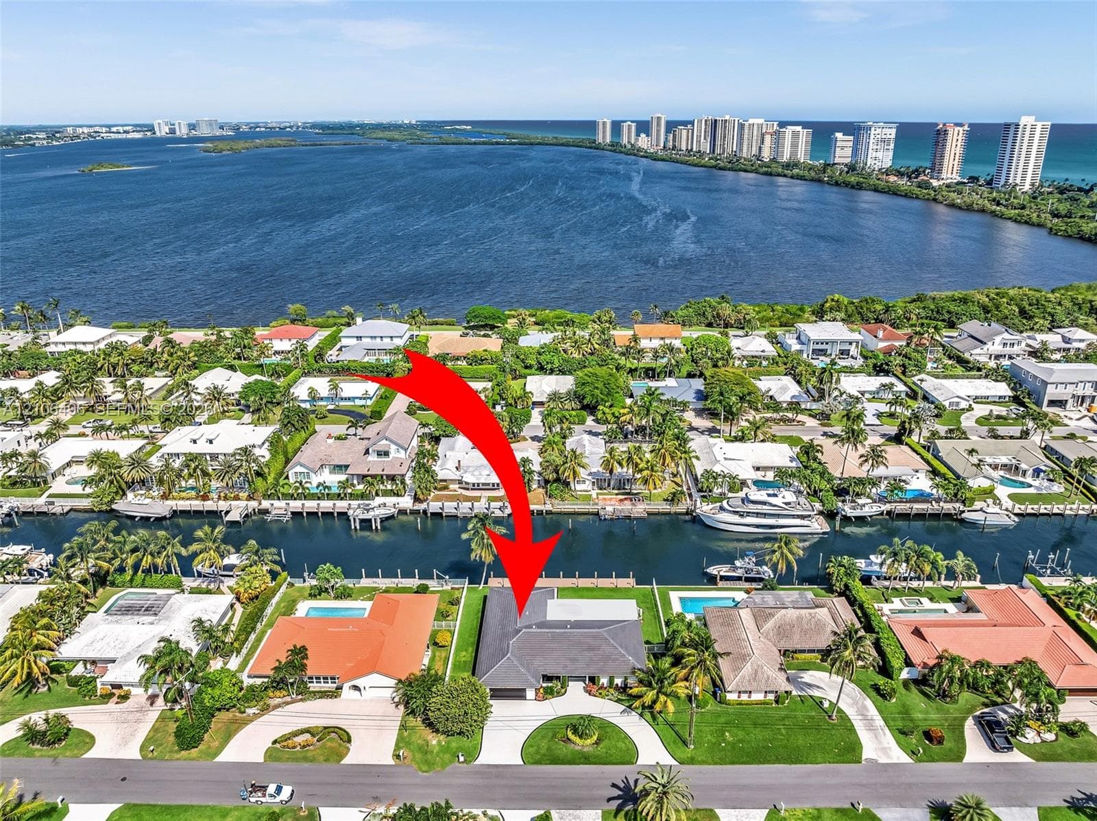 Aerial perspective of a canalfront property featuring a private boat dock, multi-pitched roofline, curved paved driveway, and mature landscaping