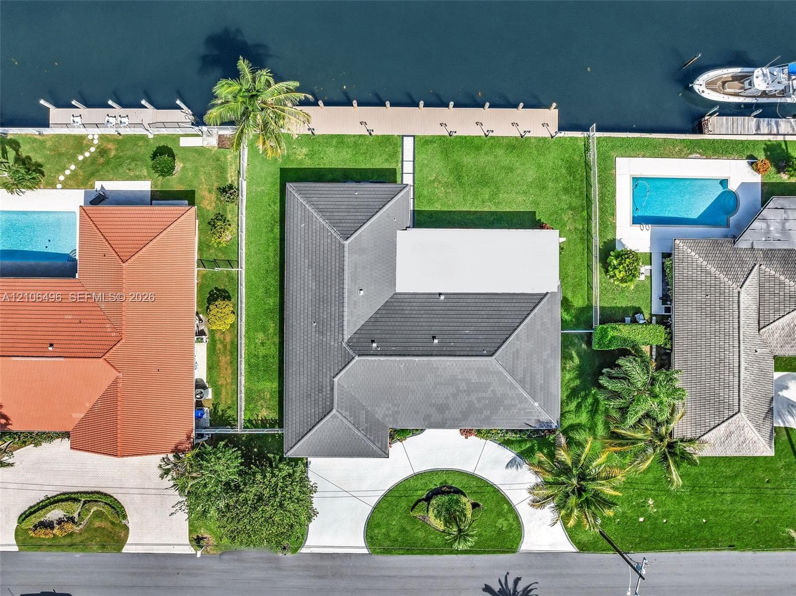 Waterfront property featuring a private dock, expansive lawn, tile roof, and a circular driveway