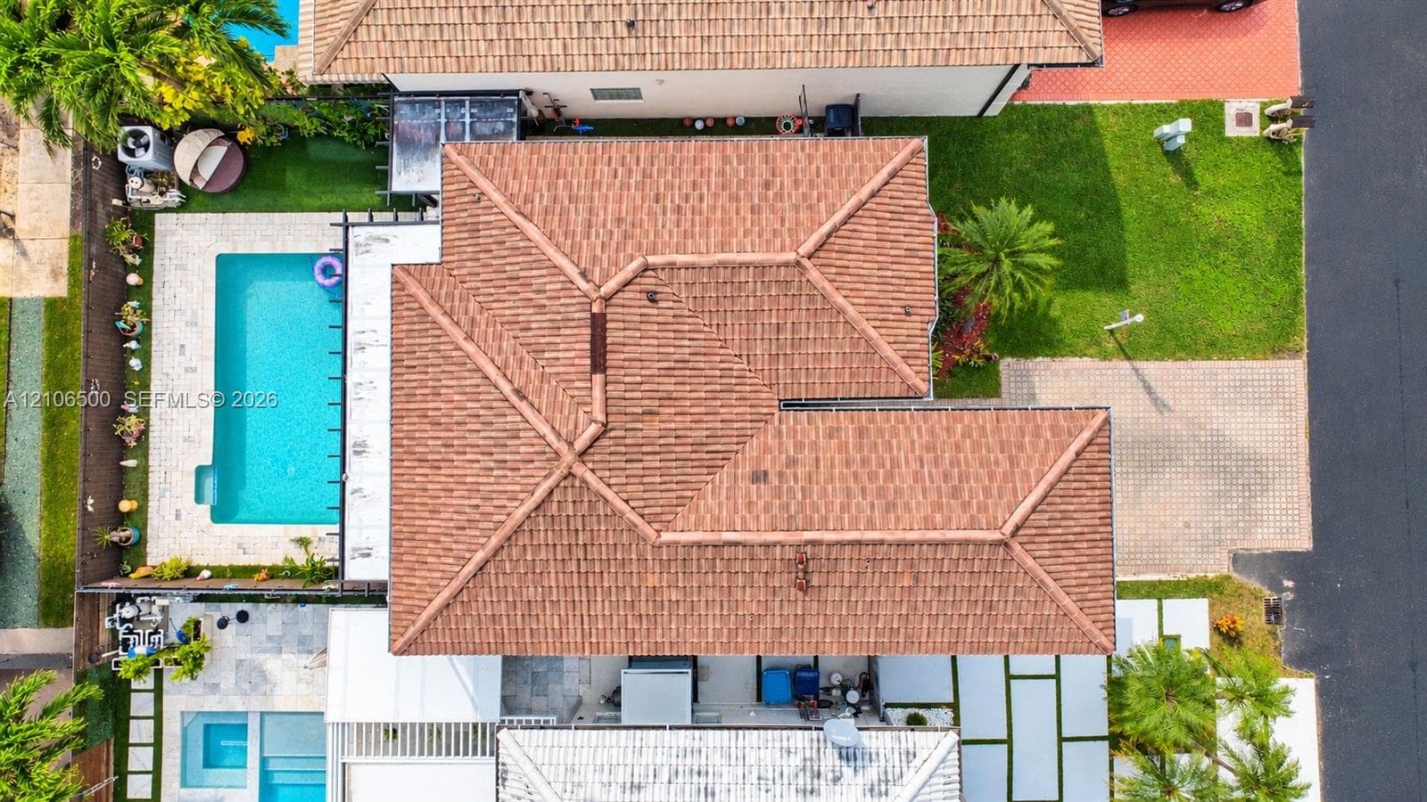 Aerial perspective featuring a multi-hipped tile roof, a rectangular in-ground swimming pool, a concrete paver driveway, and manicured turf landscaping