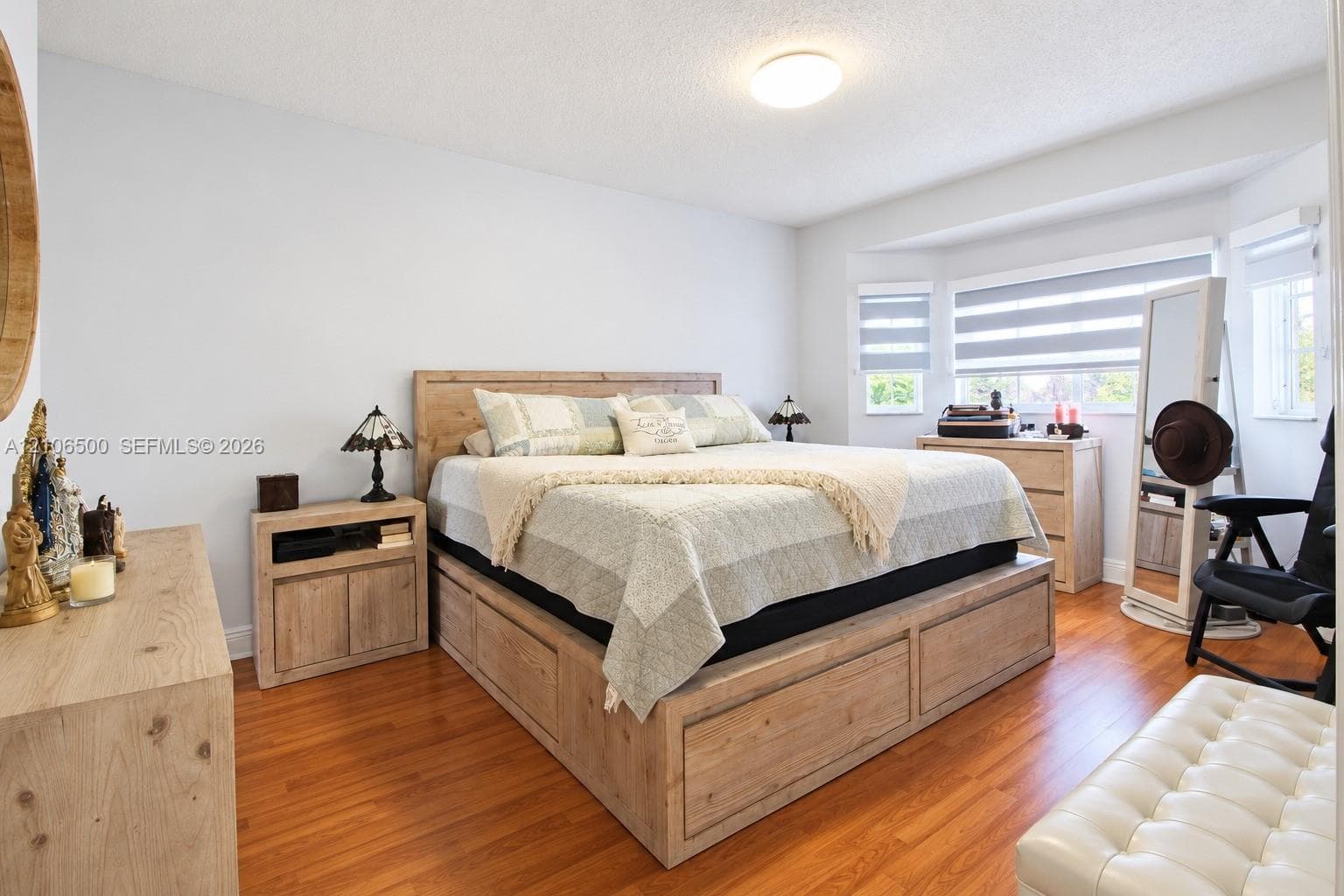 Bedroom featuring wood-finish flooring, a bay window with dual-tone roller shades, and a ceiling-mounted light fixture