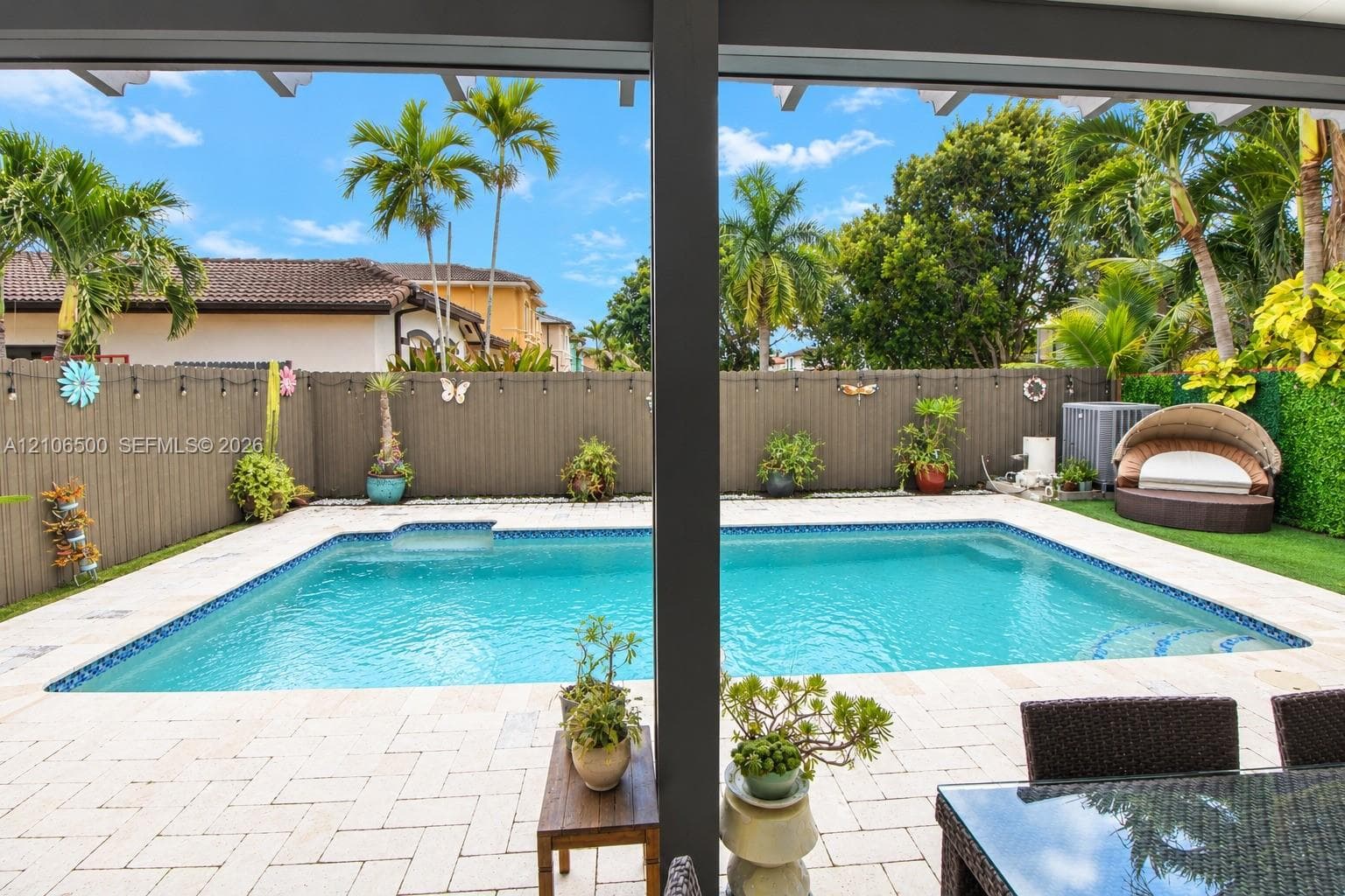 In-ground swimming pool featuring a tiled waterline, stone paver decking, privacy fencing, and an overhead structural covering
