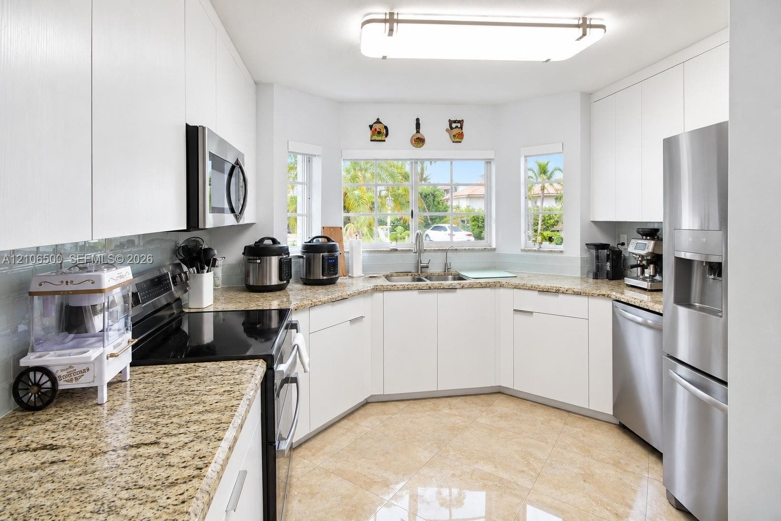 Kitchen featuring flat-panel white cabinetry, stone countertops, stainless steel appliances, dual-basin sink, and tile flooring