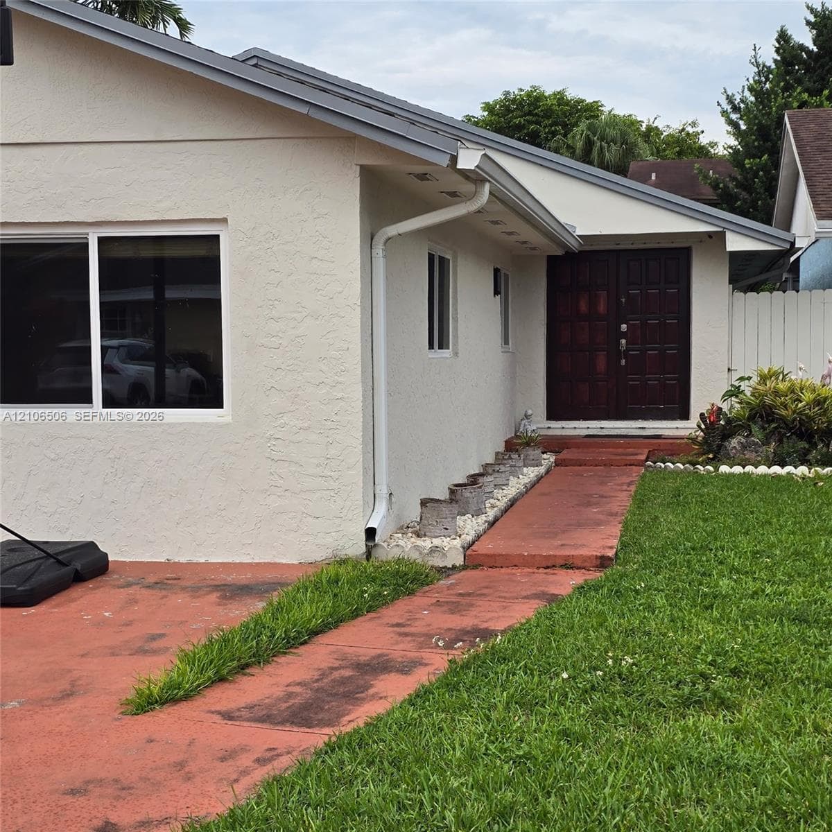Single-story exterior featuring a textured stucco finish, double-door entry with panel detailing, dual-pane windows, and a paved walkway