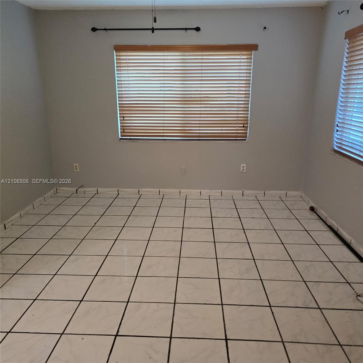 Room featuring large-format square tile flooring, neutral wall paint, and windows equipped with horizontal wood-finish blinds