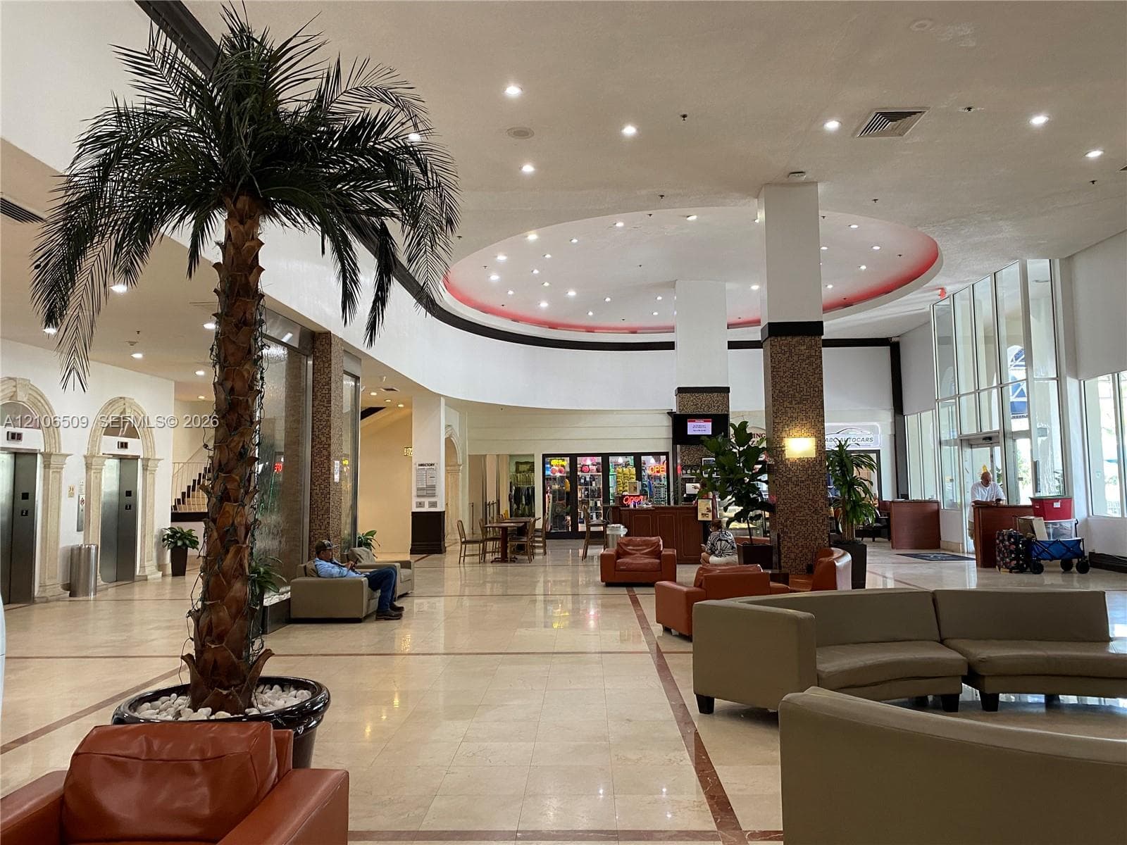Expansive lobby featuring polished stone flooring, arched elevator entrances with stone detailing, a circular recessed ceiling with integrated lighting, and full-height floor-to-ceiling windows