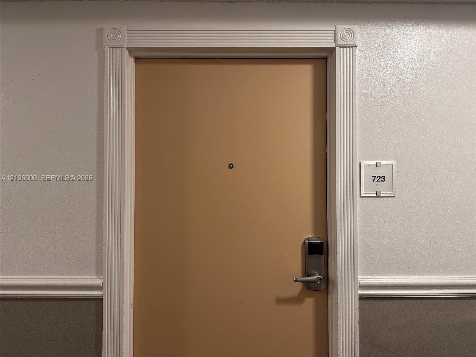 Entry door featuring fluted casing, decorative corner rosettes, a door viewer, and a digital handle lockset