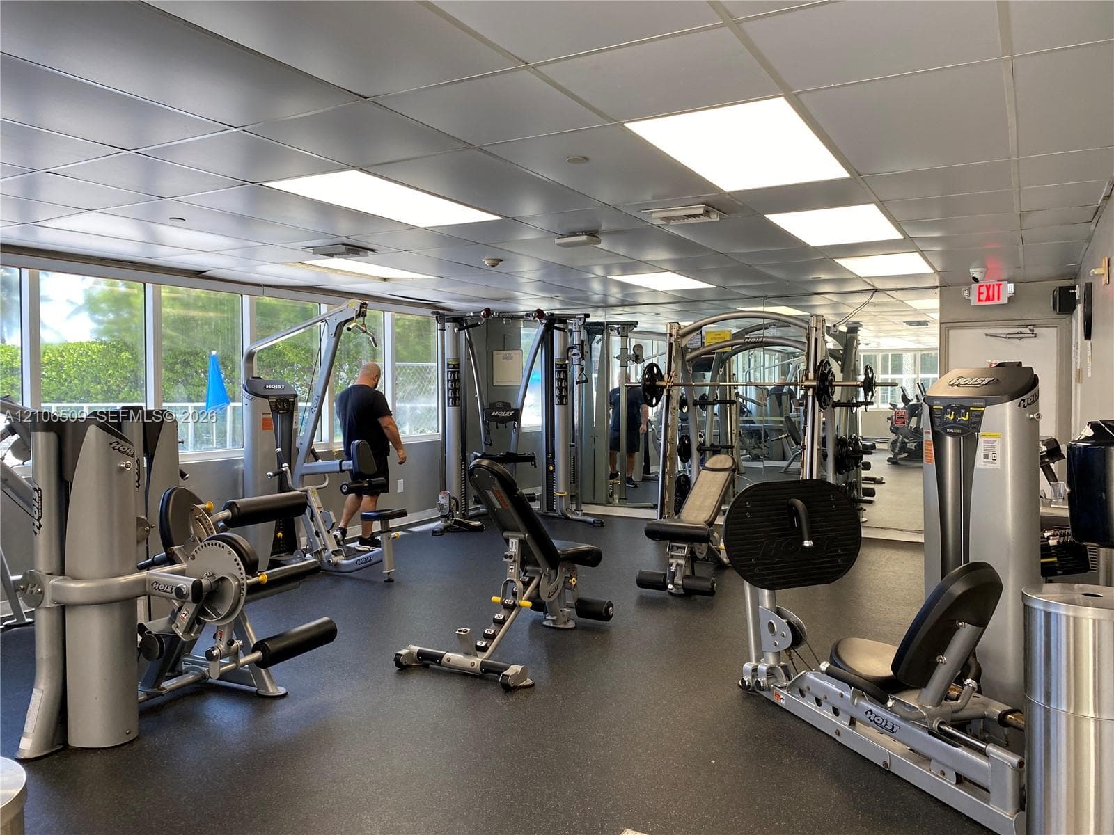 Fitness center featuring rubberized flooring, integrated ceiling panel lighting, mirrored wall surfacing, and floor-to-ceiling windows