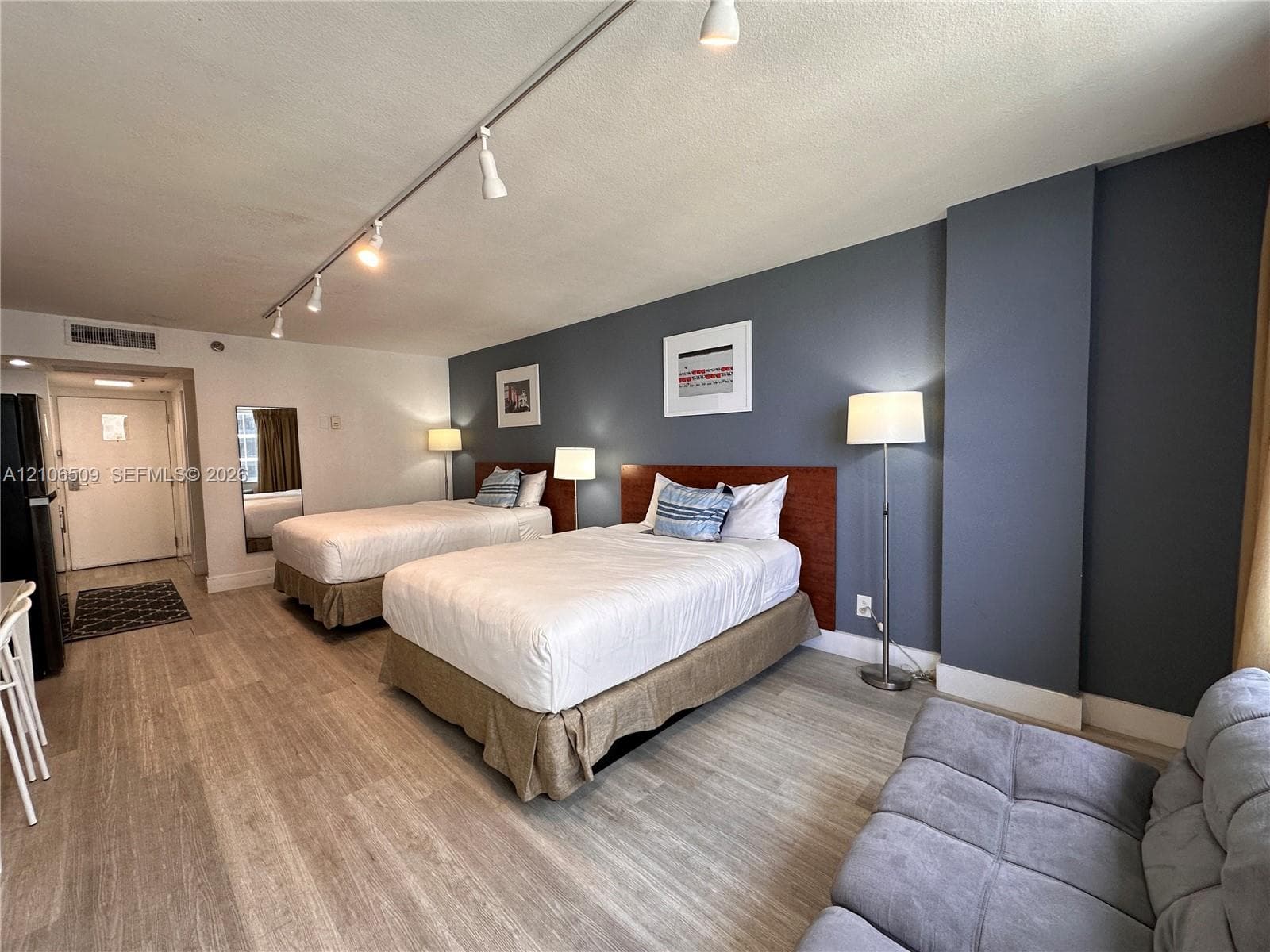 Wood-finish flooring, adjustable track lighting, built-in dark wood headboards, and a contrasting accent wall
