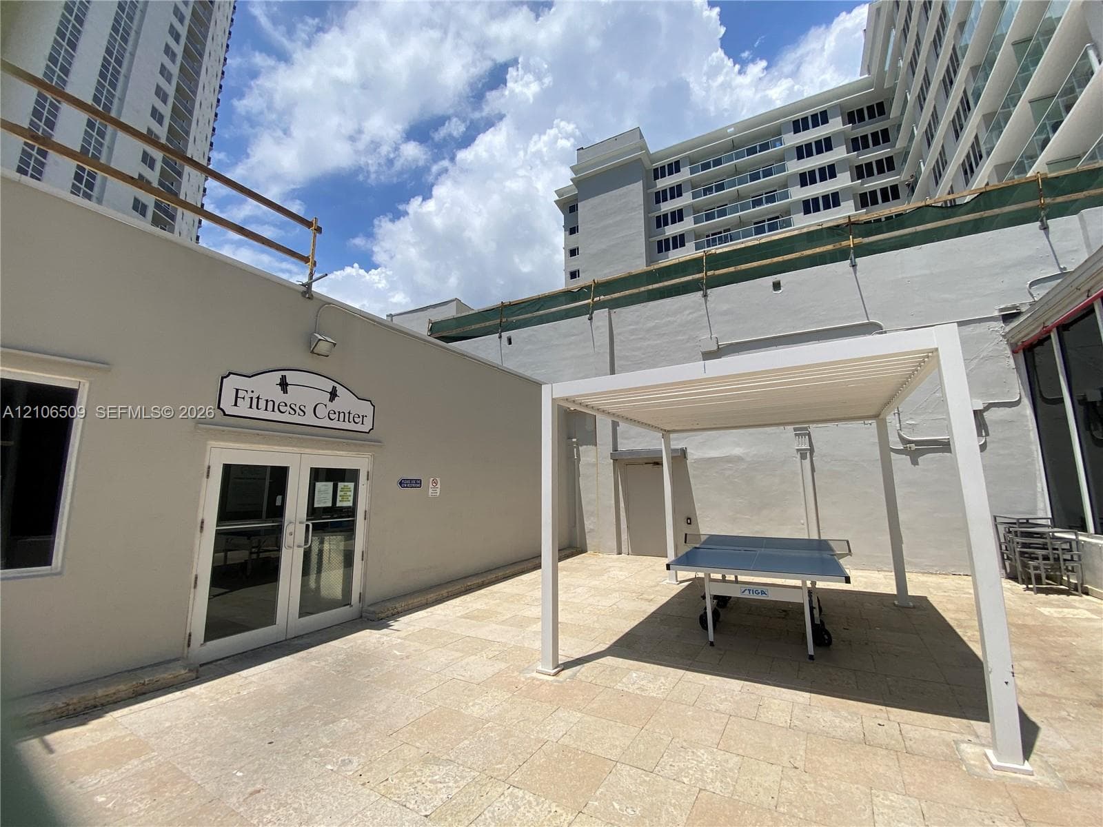 Outdoor patio featuring stone-tiled flooring, a white pergola structure, and access to a fitness center