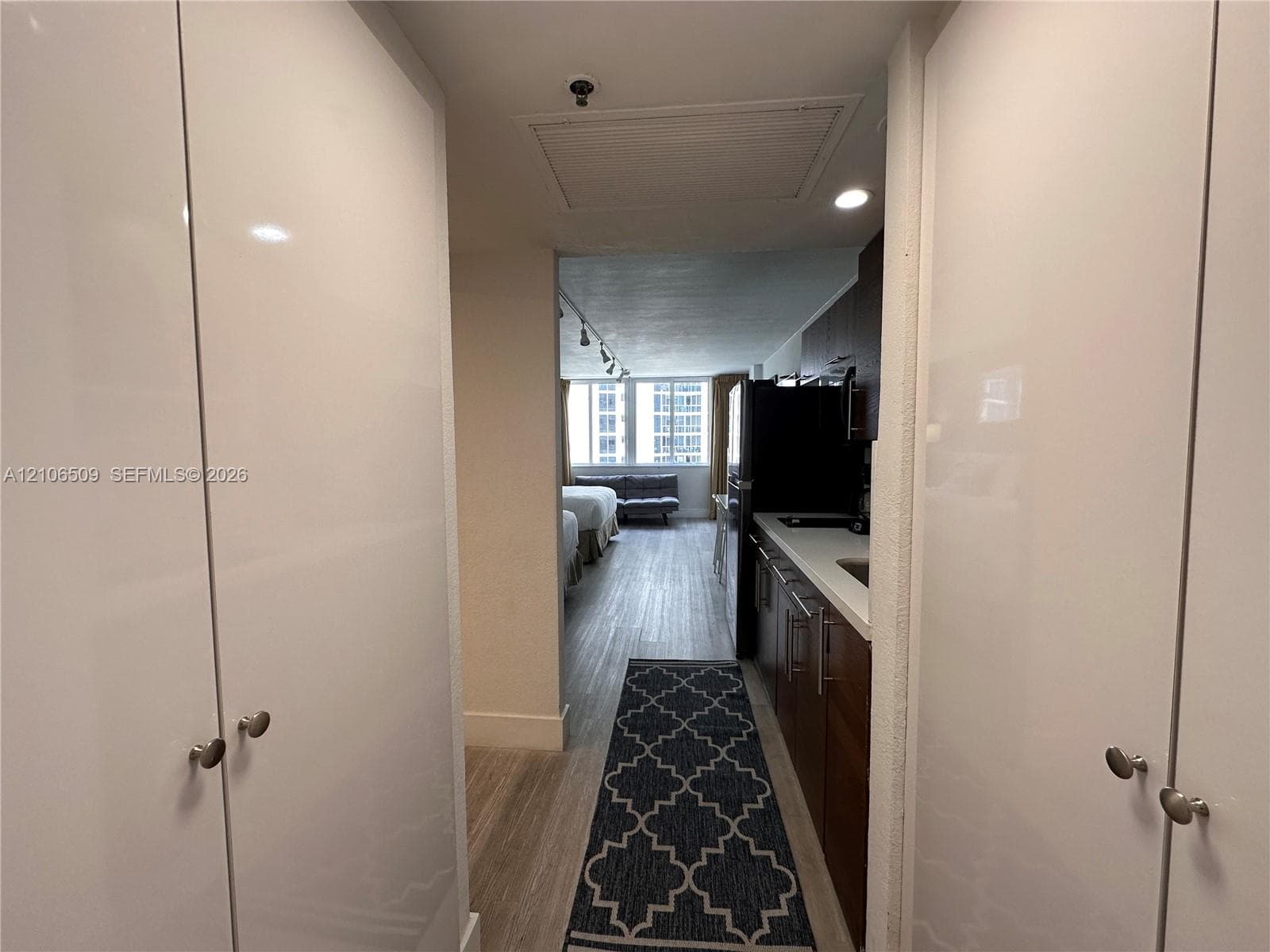 Entryway featuring dual floor-to-ceiling white cabinetry, wood-finish flooring, and galley-style kitchen with dark cabinetry and light-toned solid surface countertops