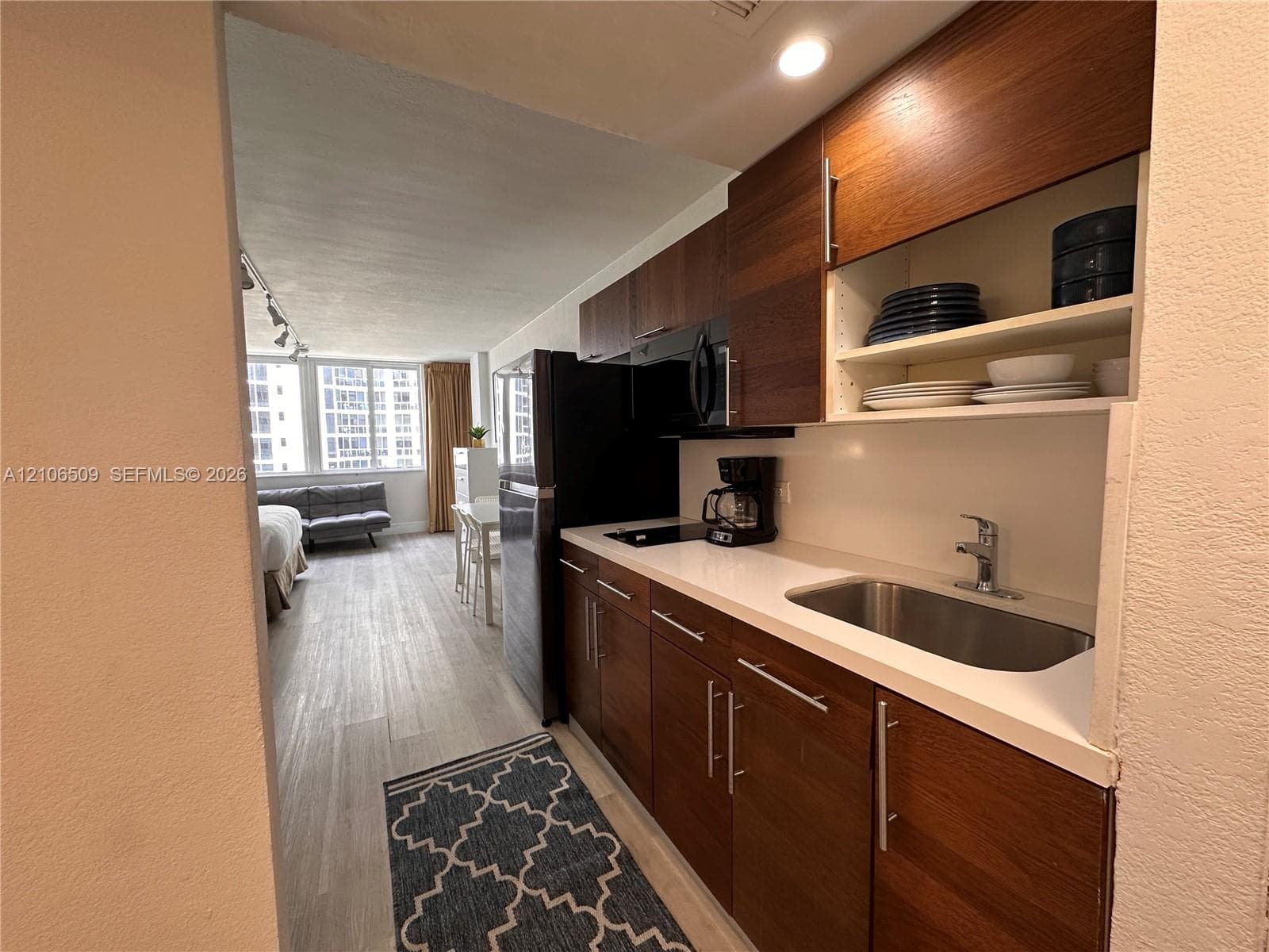 Kitchen featuring dark wood-finish cabinetry, solid-surface countertops, a stainless steel undermount sink, built-in black appliances, and wood-finish flooring
