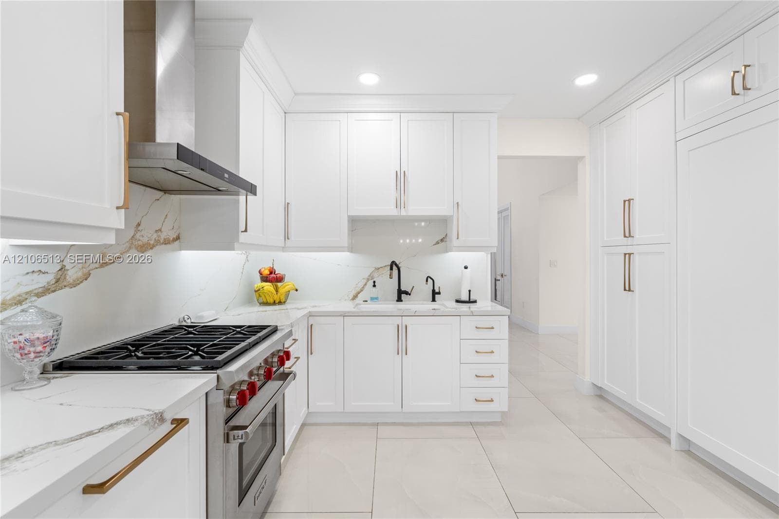 Kitchen featuring shaker-style white cabinetry, stone-finish countertops with matching full-height backsplash, stainless steel gas range with overhead vent hood, under-cabinet lighting, and large-format tile flooring