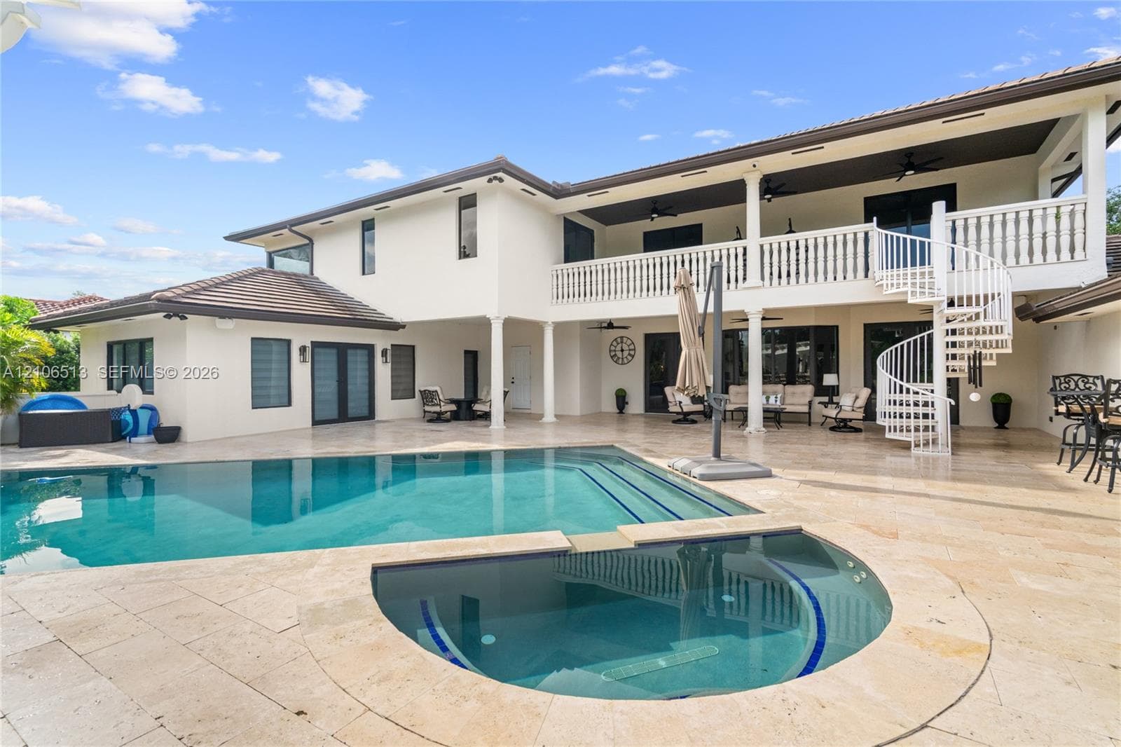 Stucco exterior featuring a dual-level covered patio, stone-finish pool deck, in-ground swimming pool with attached spa, and a white spiral staircase