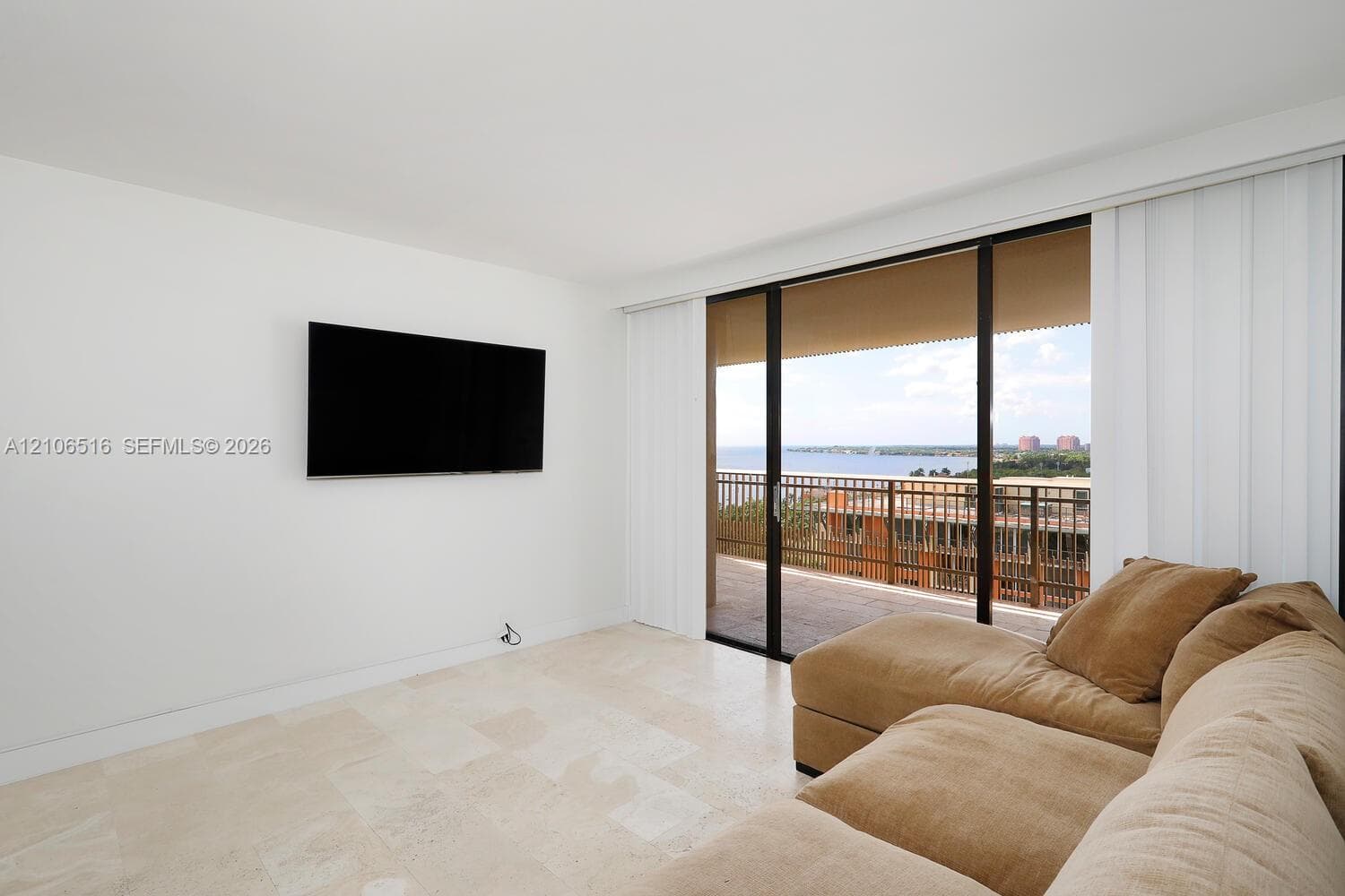 Large-format light stone flooring, floor-to-ceiling sliding glass doors, and a covered exterior balcony featuring a metal railing