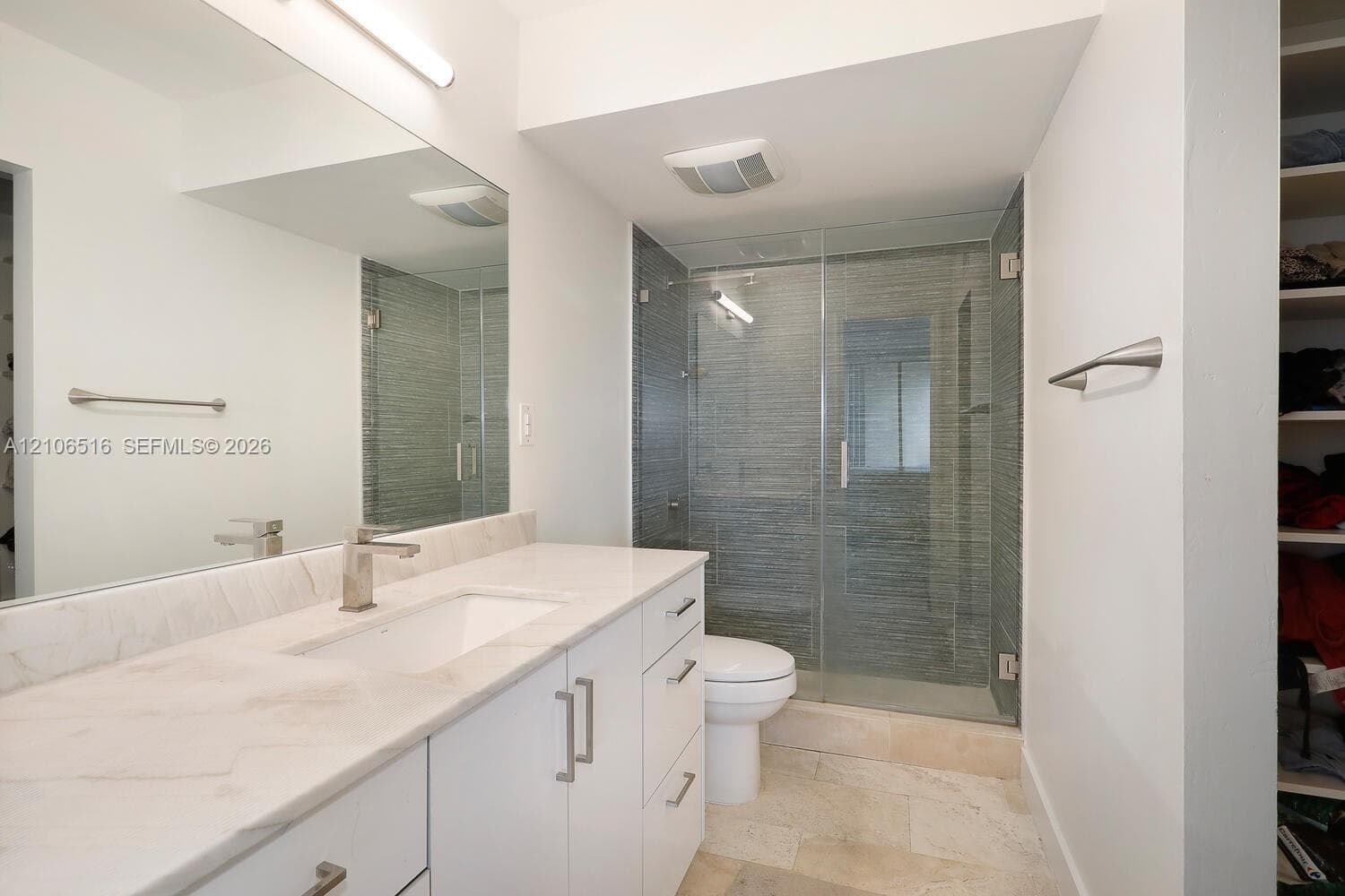 Bathroom featuring a white vanity with a stone countertop, an integrated rectangular sink, a full-width wall mirror, and a glass-enclosed shower with textured tile surround