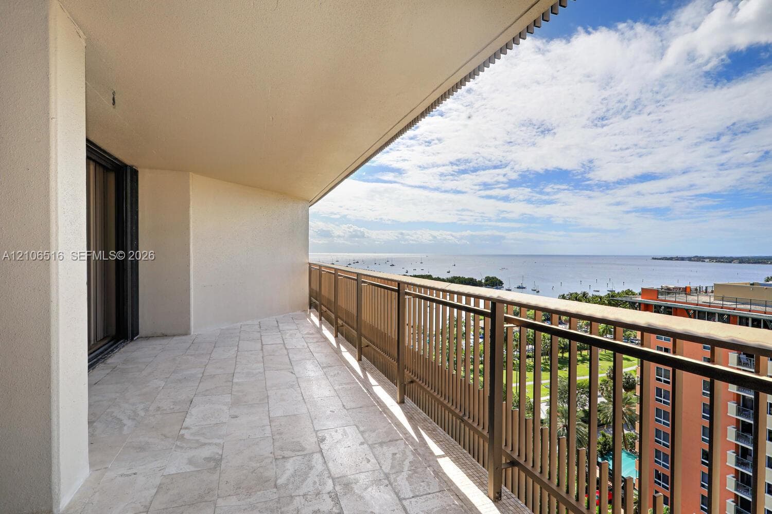 Covered balcony featuring stone flooring and metal railings, overlooking a large body of water