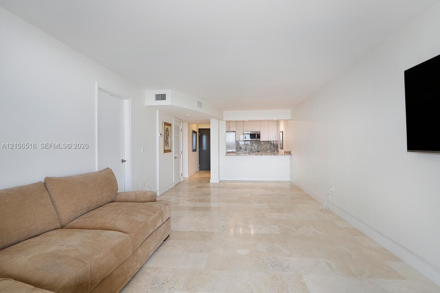 Neutral-toned stone tile flooring, smooth wall finishes, and minimalist design featuring a pass-through kitchen area with cabinetry