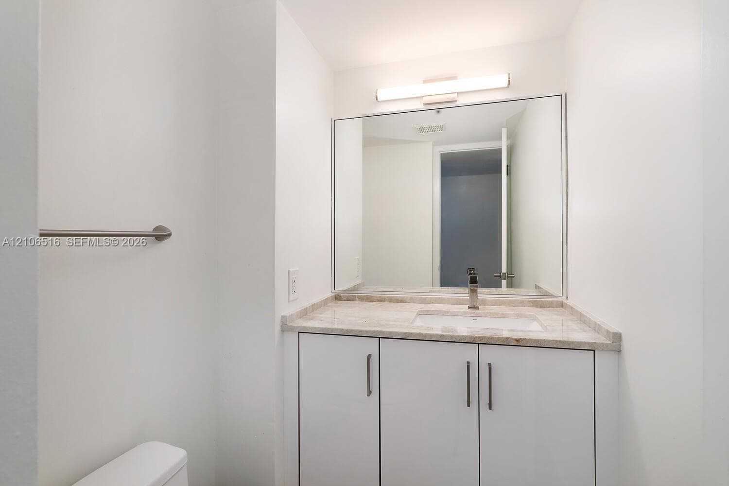White vanity cabinetry with a stone-surface countertop, rectangular undermount sink, polished metal faucet, full-width mirror, and bar-style wall lighting