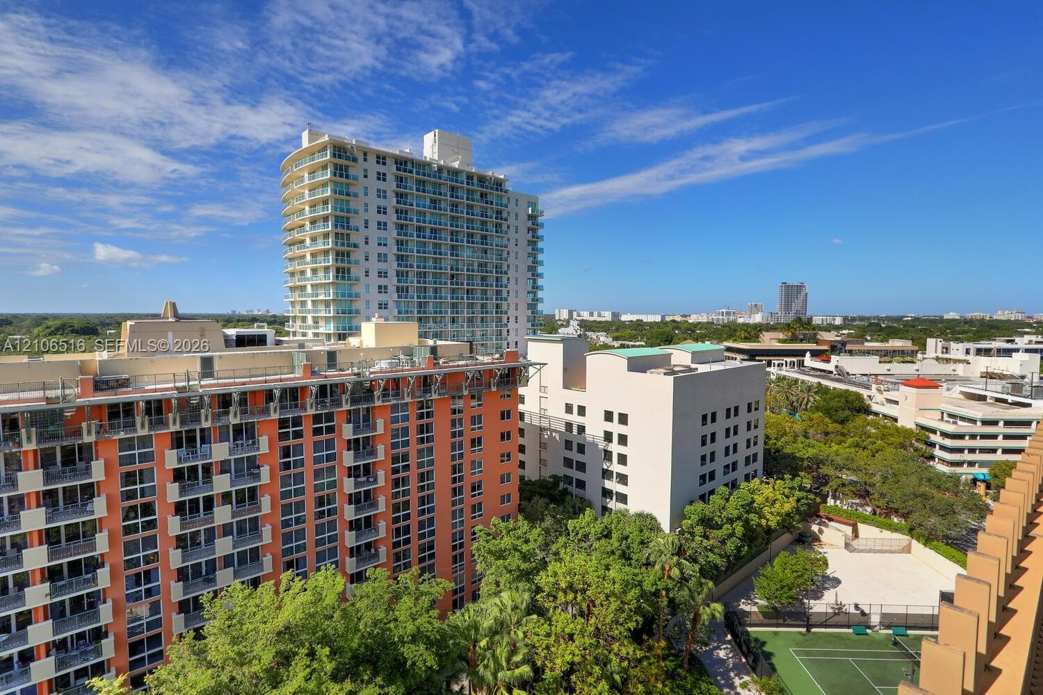 High-rise residential exterior with glass-railed balconies and a dedicated on-site tennis court nestled among mature landscaping