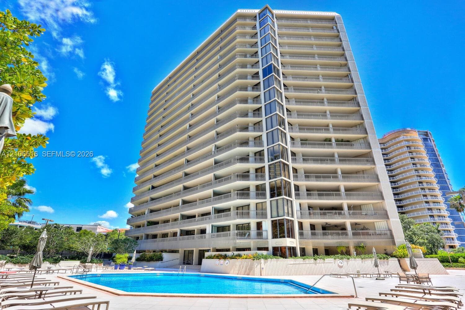 High-rise residential building featuring expansive private balconies, floor-to-ceiling glass paneling, and an outdoor swimming pool with a paved surround