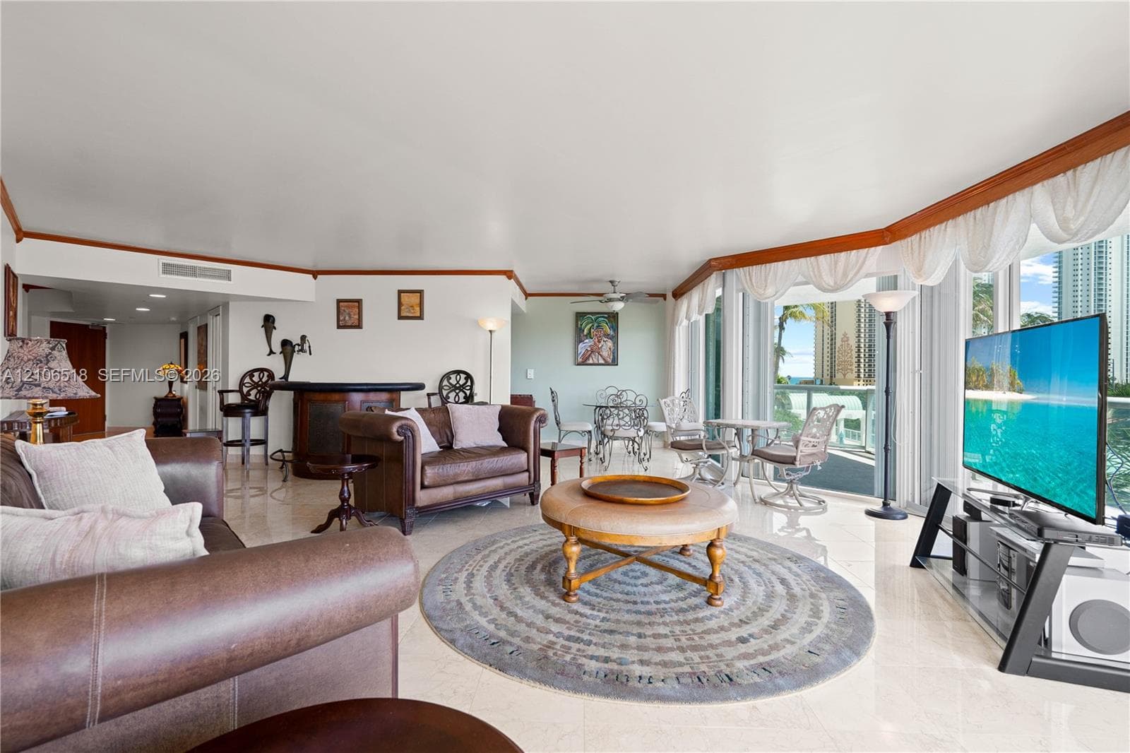 Open-concept living area featuring polished stone flooring, custom wood crown molding, a built-in wet bar, and expansive glass sliding doors leading to a balcony