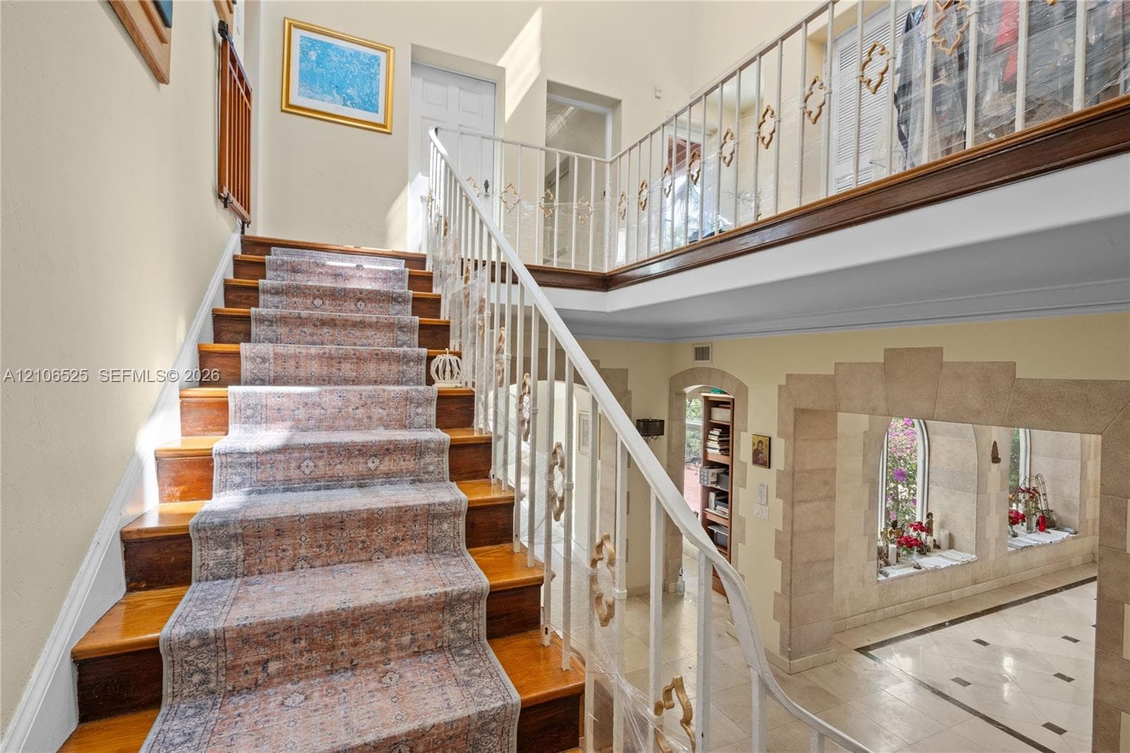 Staircase featuring wood-finish treads, decorative metal railings, and a second-level balcony overlooking a stone-accented arched entryway with tiled flooring