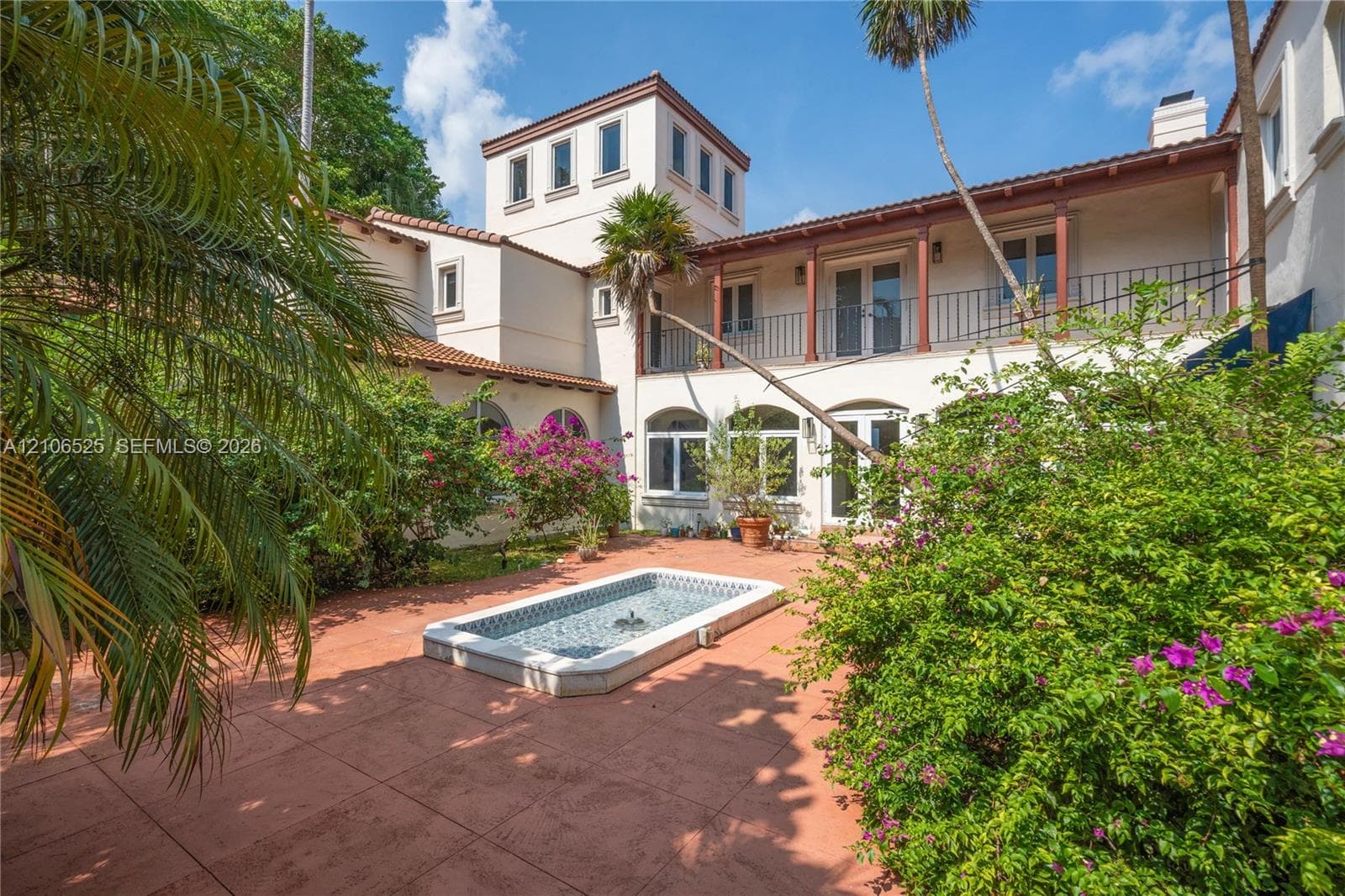 Courtyard featuring terra-cotta tile paving, a recessed water feature with decorative tile inlay, a second-story balcony with metal railing, and arched window and door openings