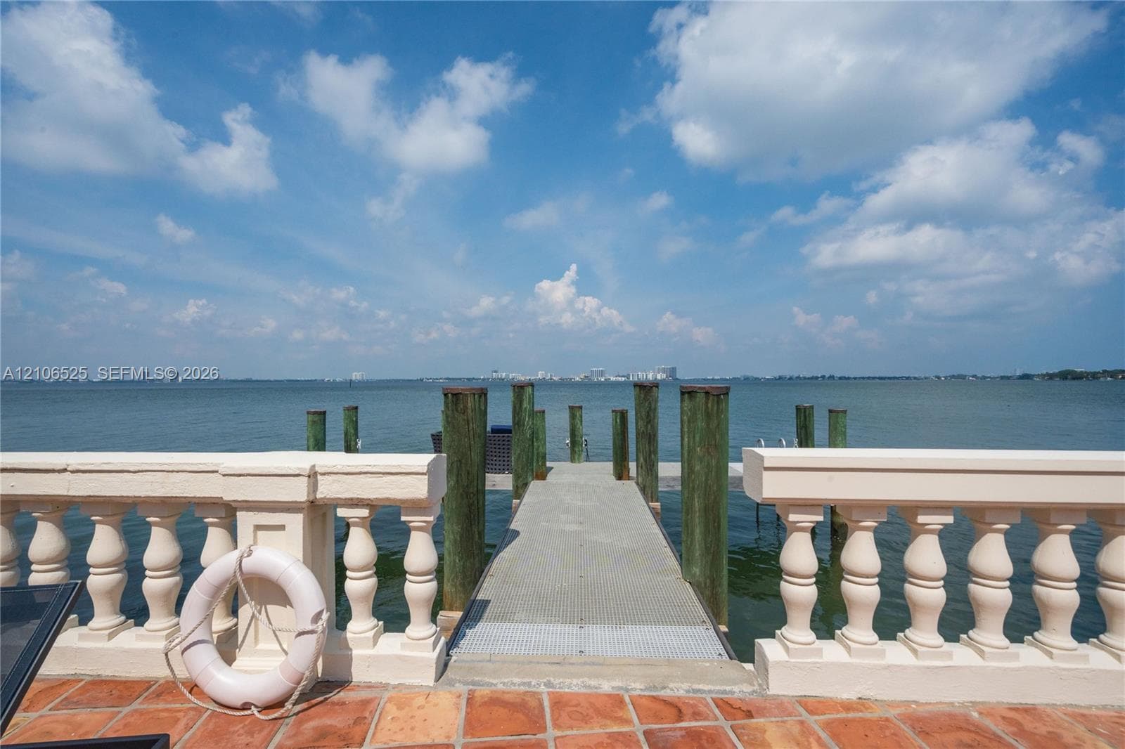 Waterfront property featuring a private dock with pilings, stone-paved patio, and classic balustrade railing