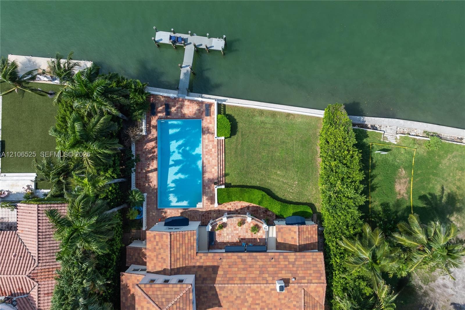 Waterfront property featuring a rectangular swimming pool, terracotta-tiled patio, private boat dock, and manicured lawn