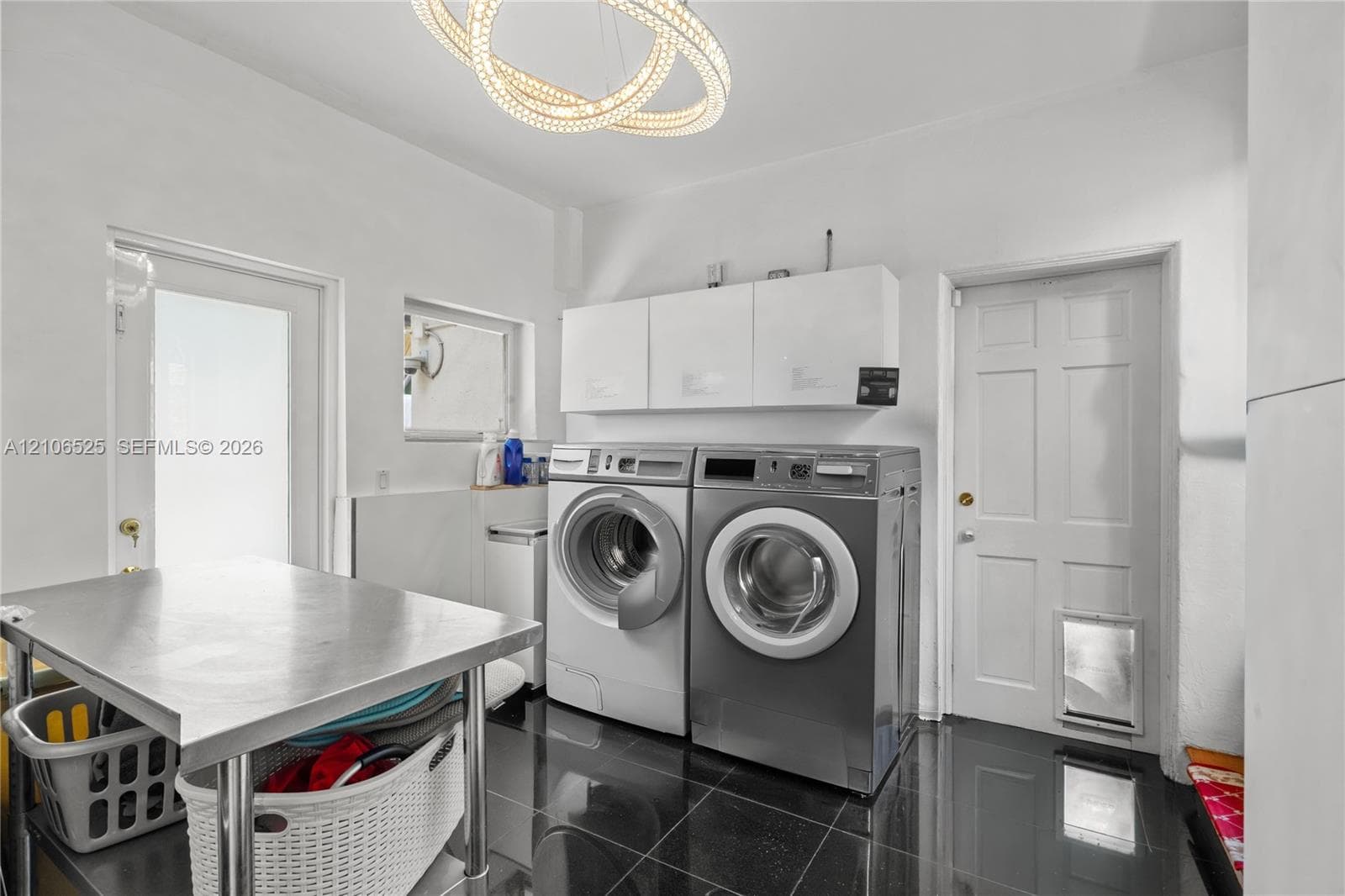 Utility room featuring polished dark tile flooring, white wall-mounted storage cabinetry, a contemporary circular dual-ring chandelier, and a six-panel exterior door with a built-in pet portal